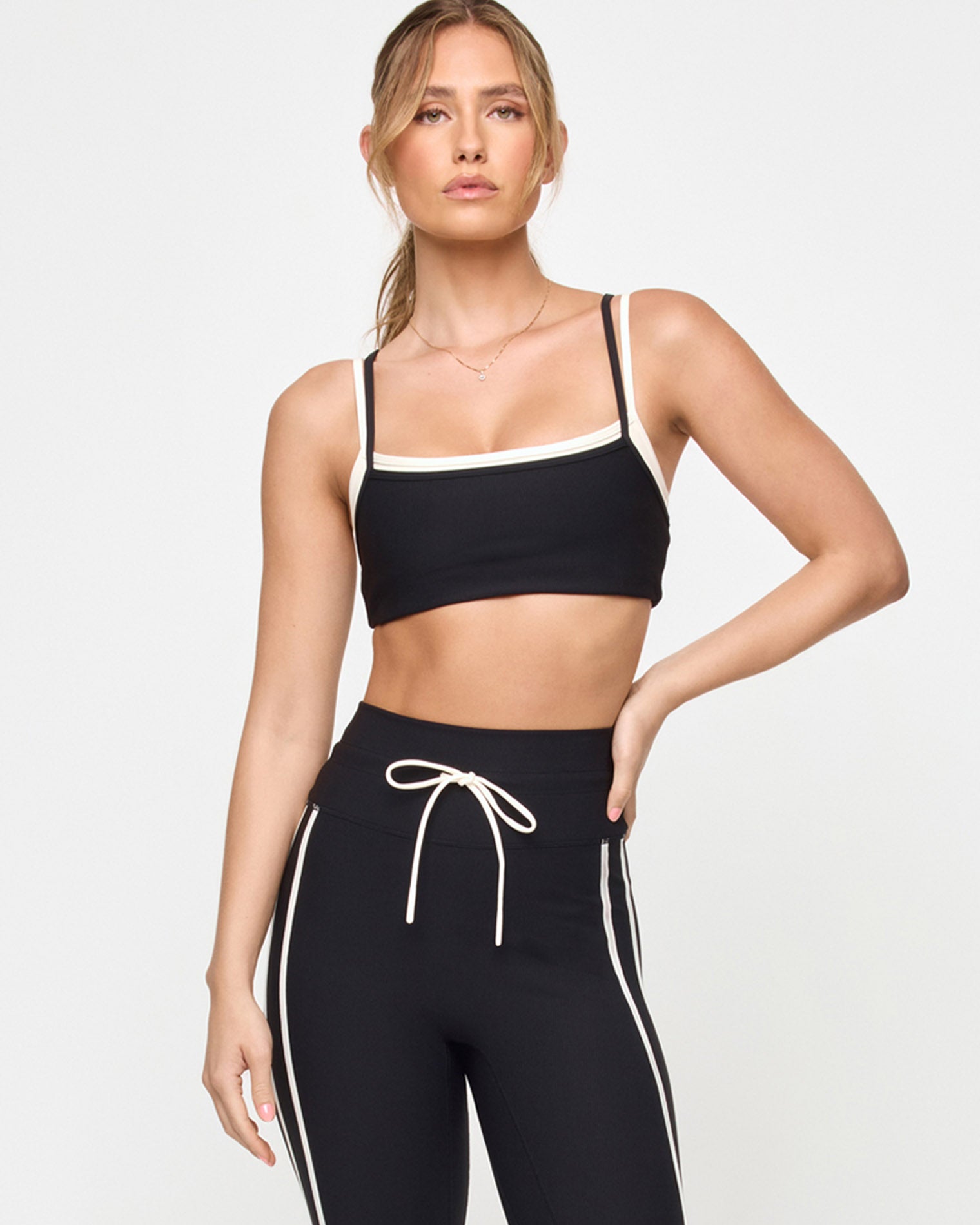 Kelly Bra - Black-Cream Front view of the LSPACE Kelly Bra in black-cream on a model against a light background, showing the sports bra design with cream trim detail, paired with black-cream high-rise active pants.