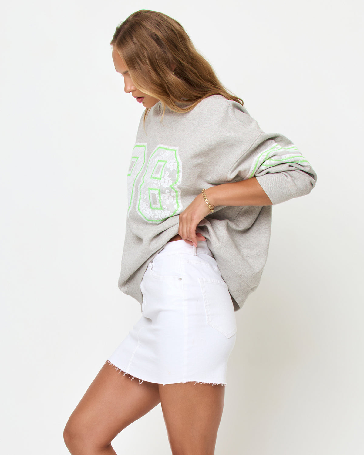 Legend Sweatshirt - Limeade Angled side studio view of the Legend Sweatshirt in Limeade, a heather gray oversized crewneck sweatshirt with a neon green graphic, styled with a white denim skirt.