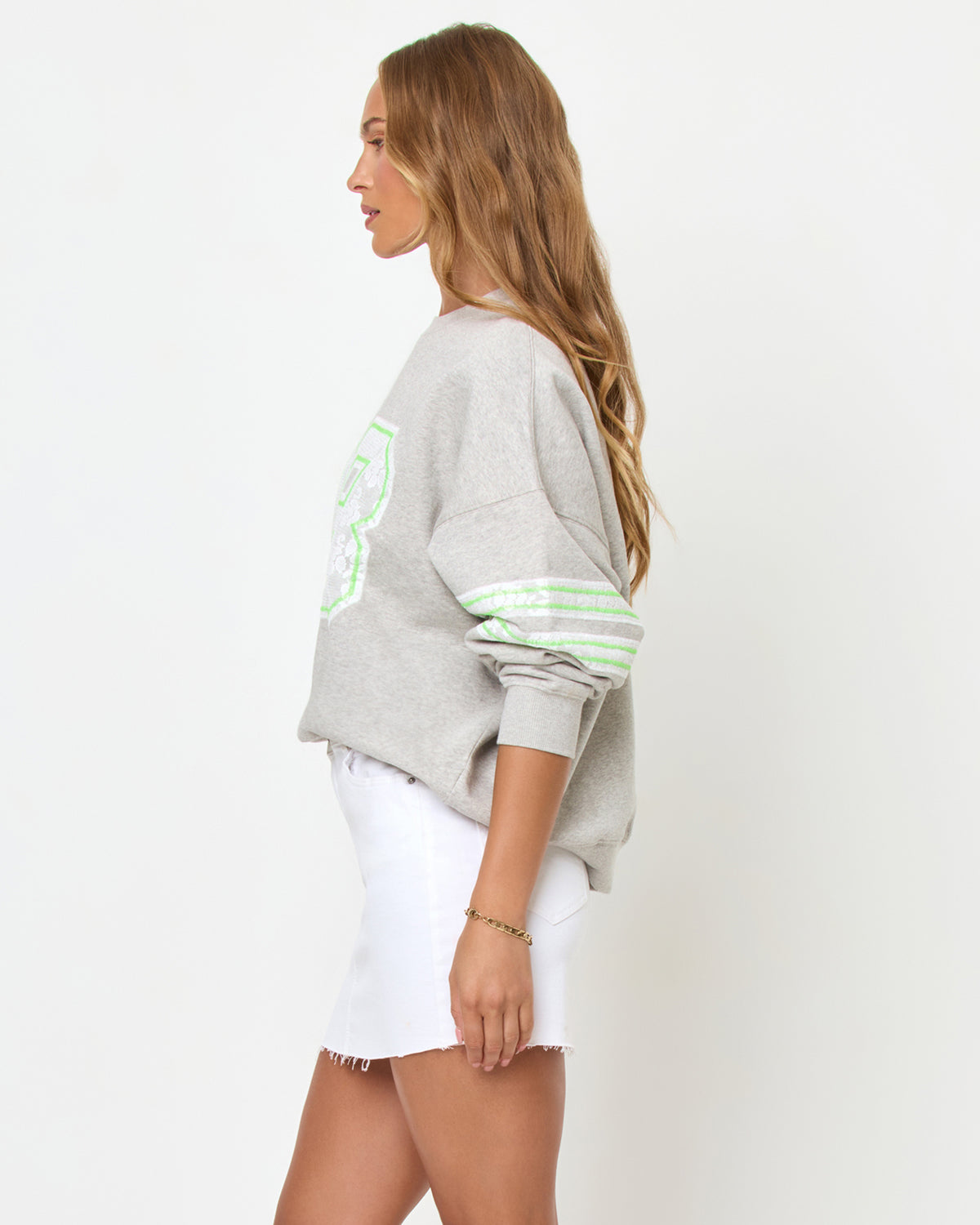 Legend Sweatshirt - Limeade Side three-quarter studio view of the Legend Sweatshirt in Limeade, a heather gray oversized crewneck sweatshirt with a neon green graphic, styled with a white denim skirt.