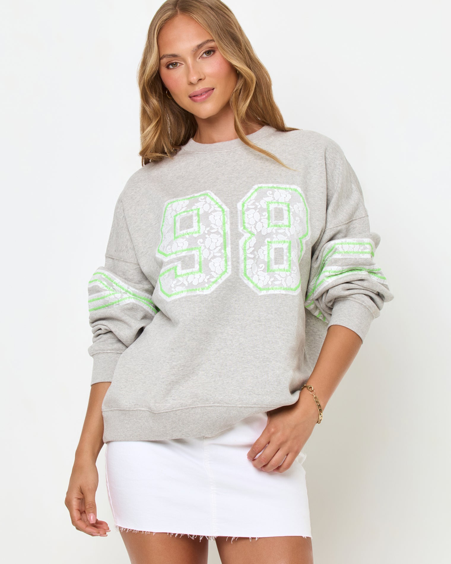 Legend Sweatshirt - Limeade Front studio view of the Legend Sweatshirt in Limeade, a heather gray oversized crewneck sweatshirt with a neon green "98" graphic on the chest, styled with a white denim skirt.