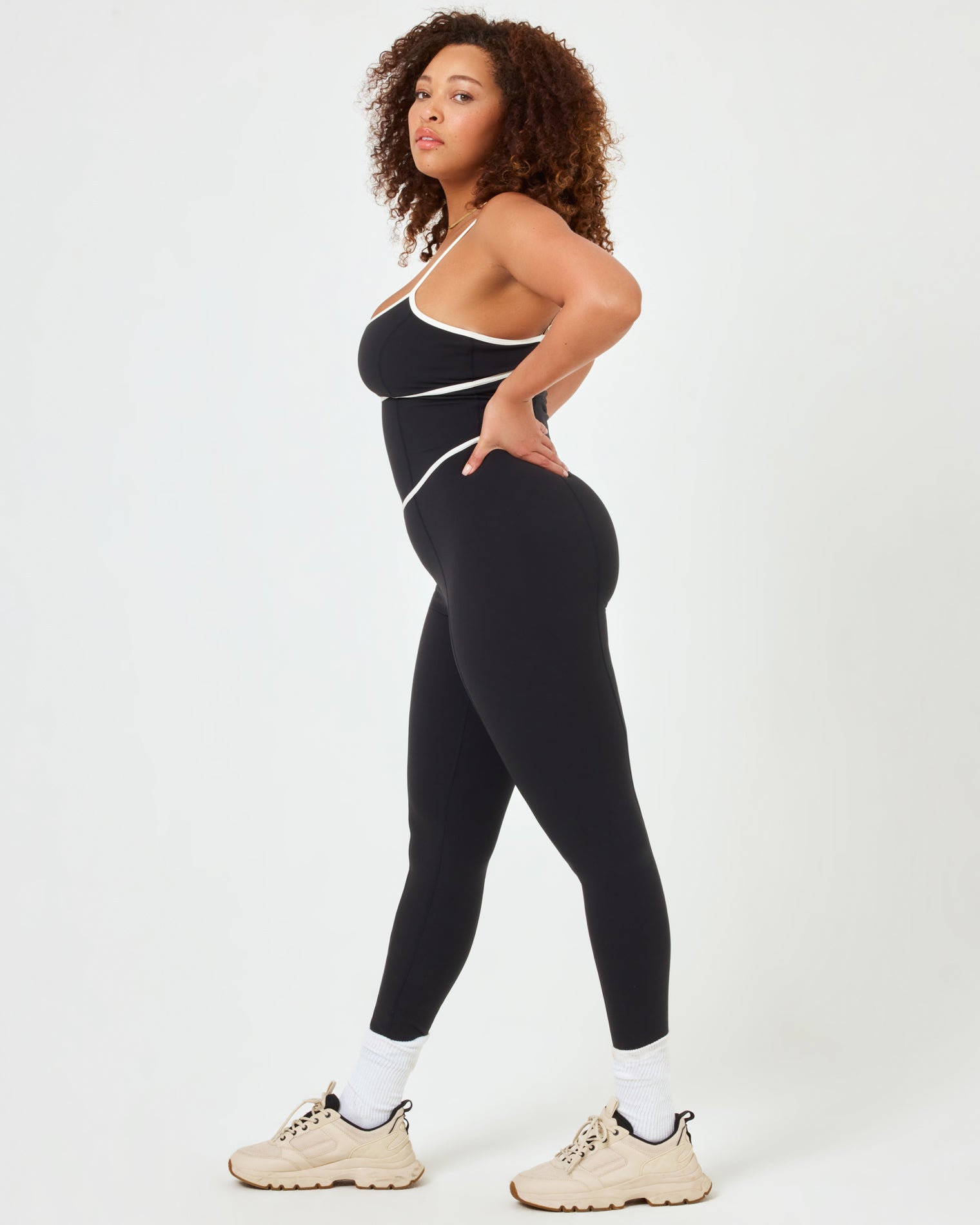 Ace Jumpsuit - Black-Cream Side view of plus size model wearing the Ace Jumpsuit in black-cream showing the side cutout and cream contrast piping.
