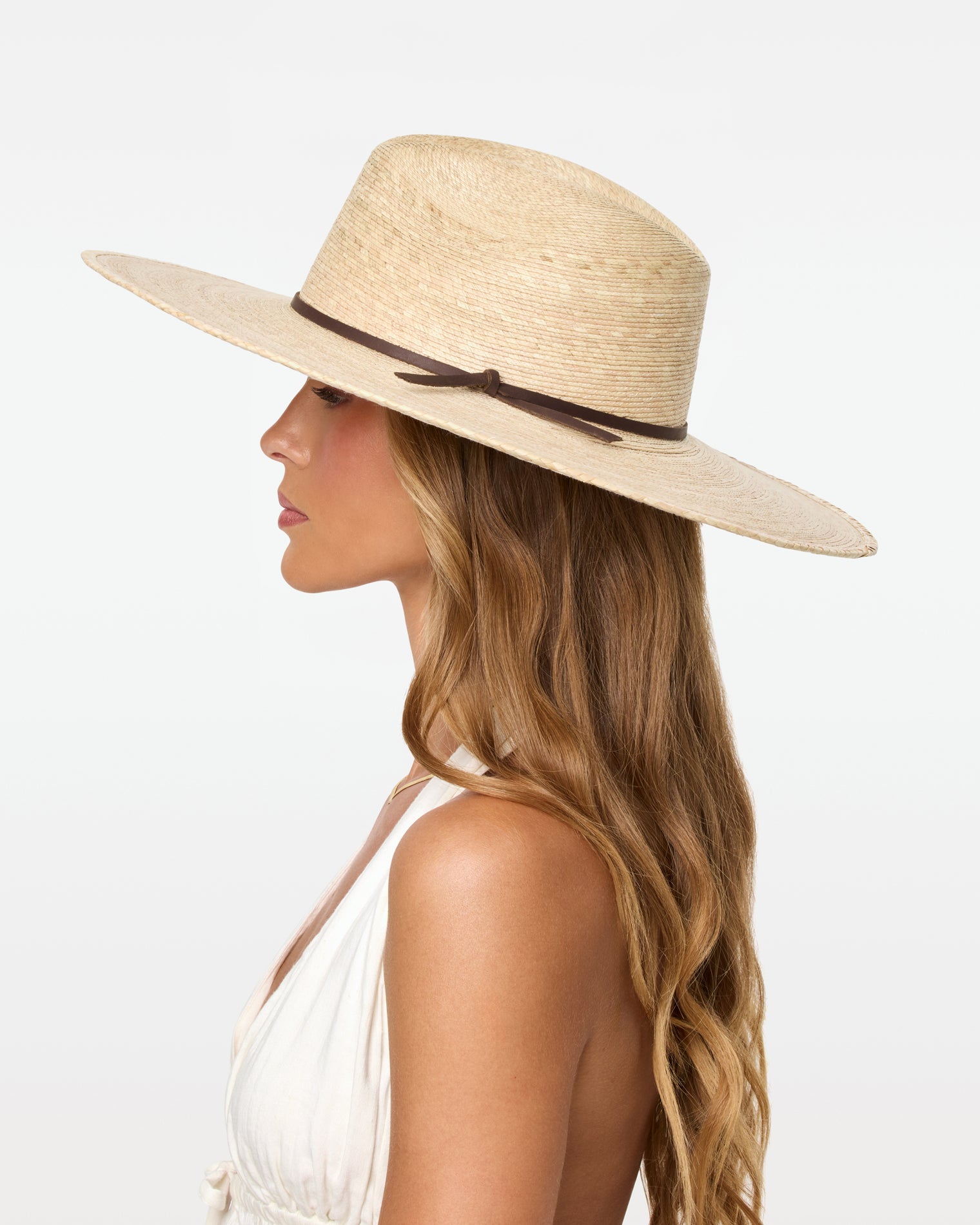 Isla Hat - Natural Side profile view of a model wearing the natural Isla Hat with a white halter top, showing the wide brim and dark cord band detail.