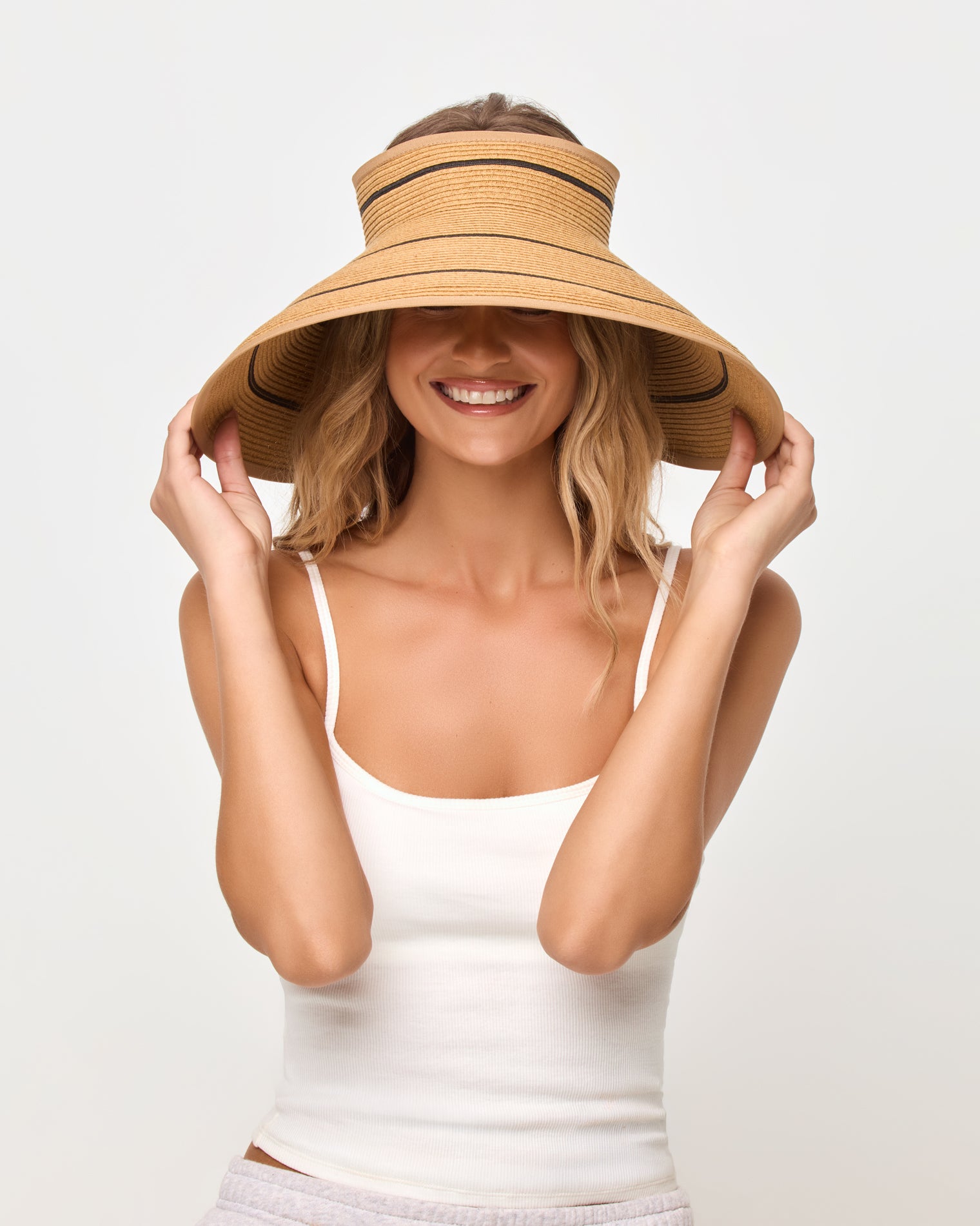 Jess Roll Up Hat - Natural-Black Front view of a smiling model pulling the brim of the natural and black Jess Roll Up Hat down over her eyes, wearing a white tank top.