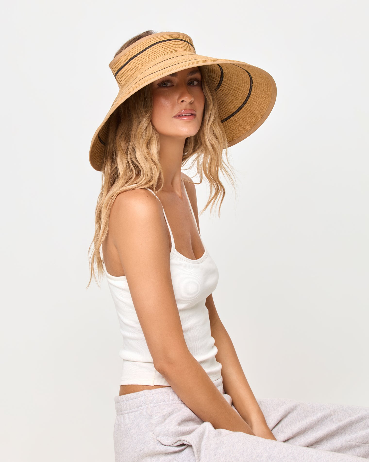 Jess Roll Up Hat - Natural-Black Side view of a model wearing the natural and black Jess Roll Up Hat with a white tank top and grey sweatpants, seated.