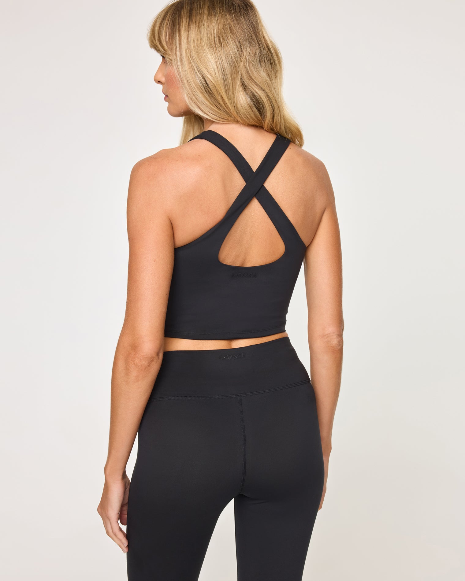 Declan Top - Black Back view of model wearing the Declan Top in black showing the crossback strap detail with cutout, with black flare legging.