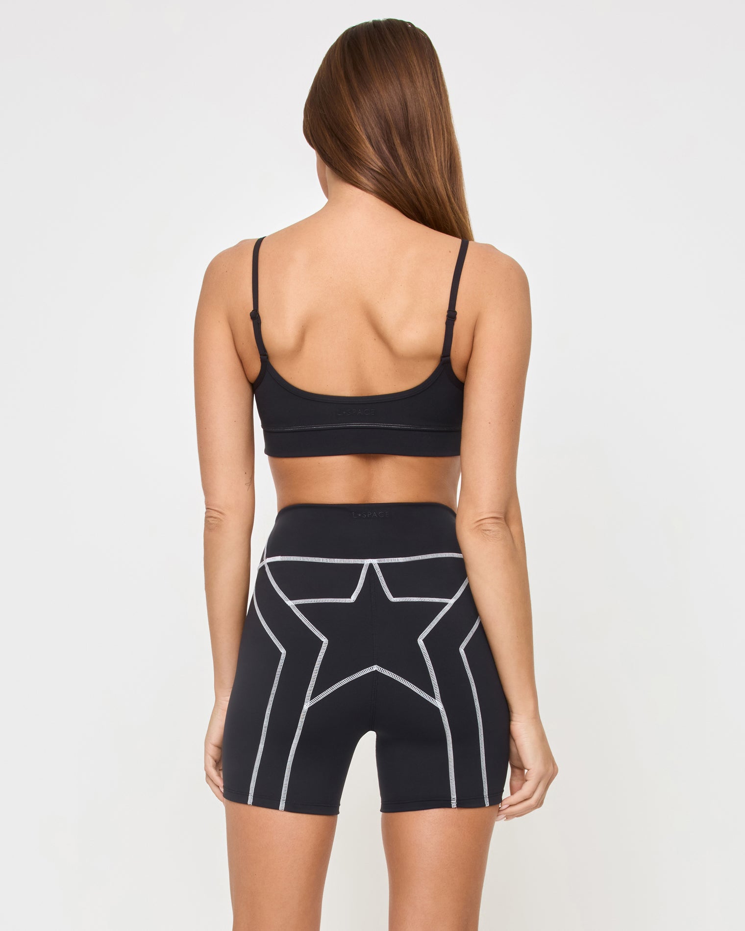 Star Power Shorts - Black Back view of the LSPACE Star Power Shorts in black on a model against a white background, showing the white star and lightning bolt graphic on the seat of the bike shorts, paired with the matching black Eclipse Bra.