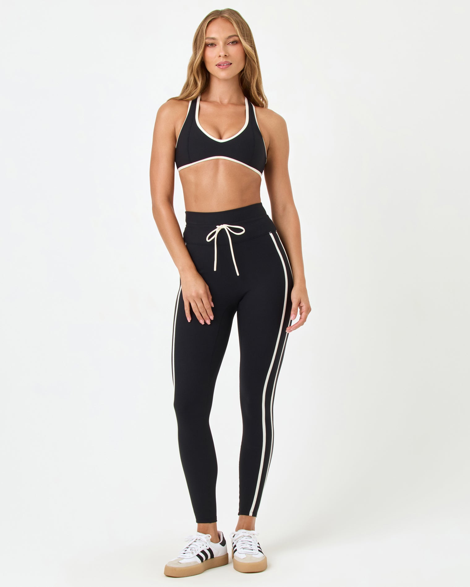 Finley Bra - Black-Cream Front view of the LSPACE Finley Bra in black-cream on a model against a white background, showing the full halter-style sports bra with cream trim, paired with black high-rise active pants with cream stripe.