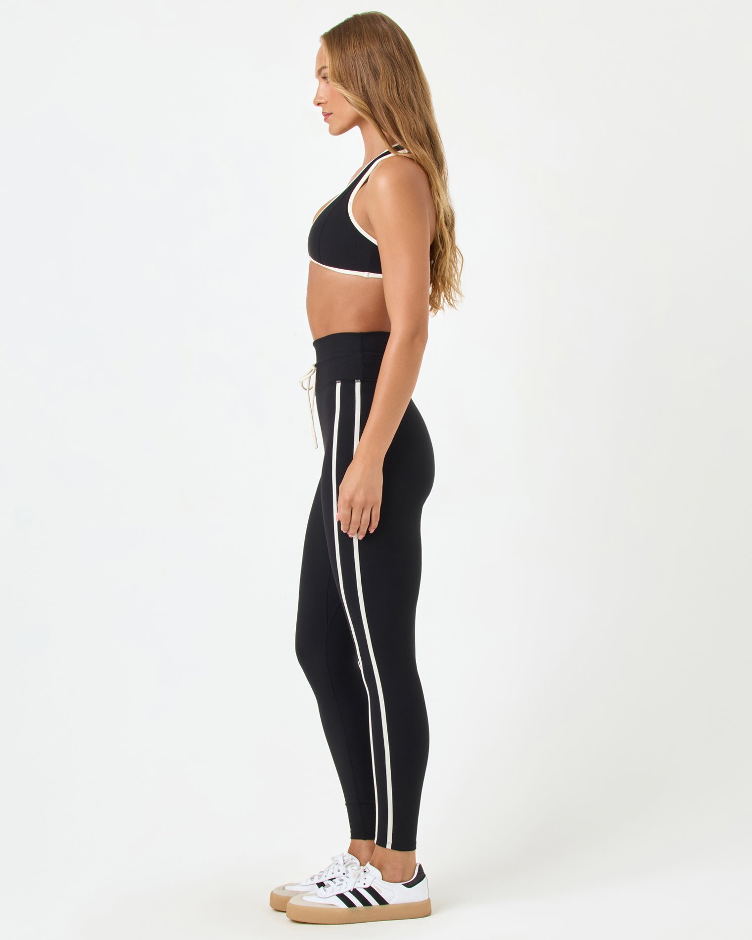 Finley Bra - Black-Cream Side view of the LSPACE Finley Bra in black-cream on a model against a white background, paired with black high-rise active pants with cream trim, showing the profile silhouette.