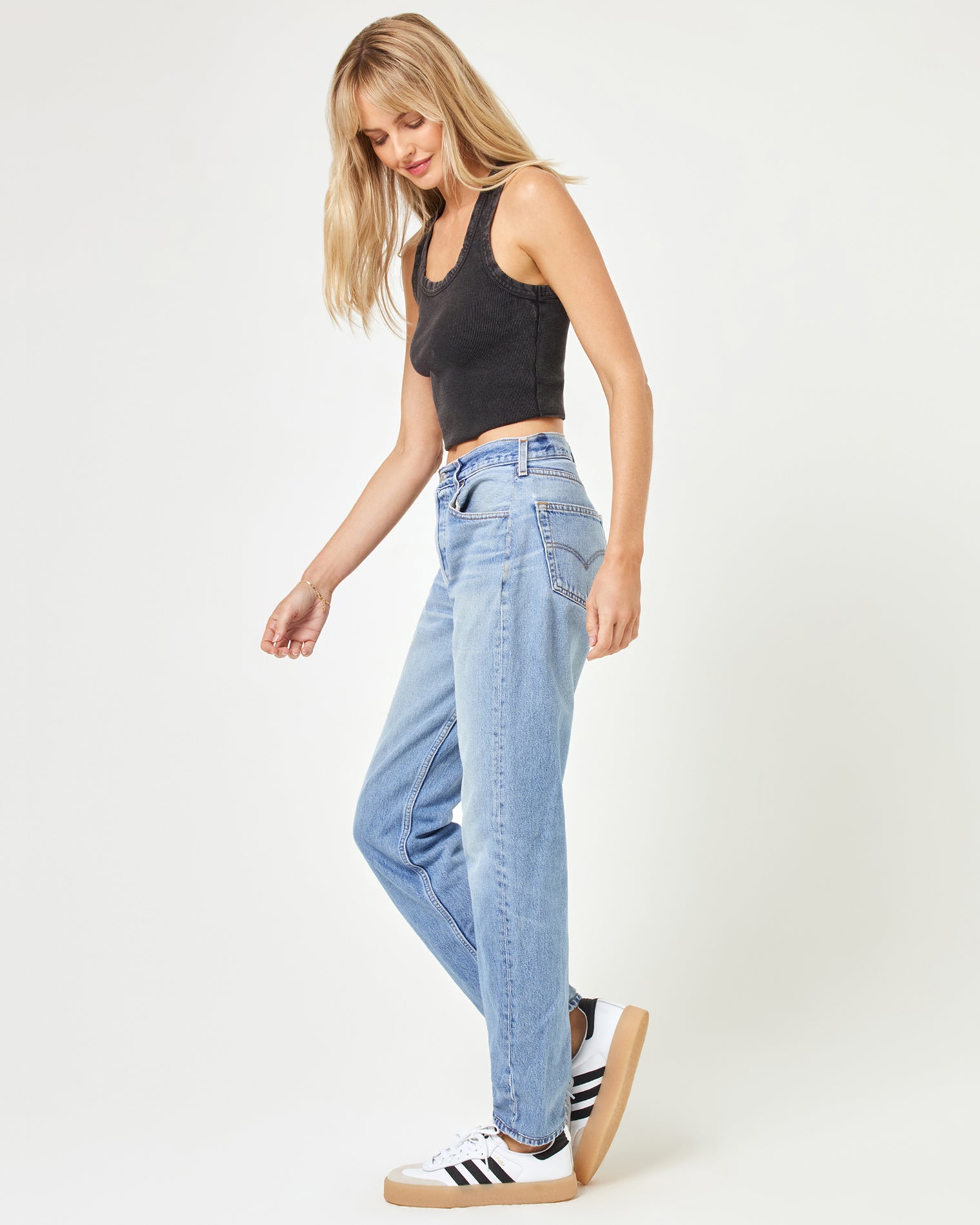 aligrace Brigette Baggy Denim Pant Side walking view of a model wearing the LSPACE aligrace Brigette Baggy Denim Pant in blue, looking down, styled with a black ribbed crop tank and sneakers.