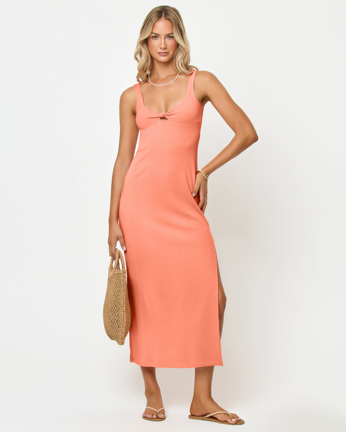 Alexis Dress - Fresh Squeezed Front view of a model wearing the LSPACE Alexis Dress in fresh squeezed, a fitted ribbed midi dress in peach with thick straps, a sweetheart neckline, front knot detail, and side slit.