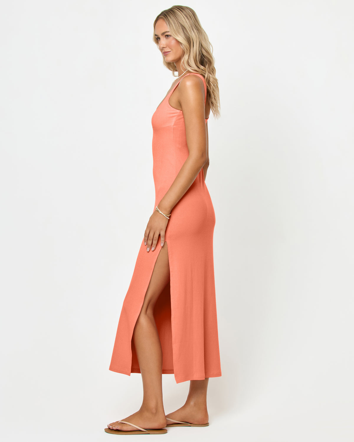 Alexis Dress - Fresh Squeezed Side view of a model wearing the LSPACE Alexis Dress in fresh squeezed, showing the fitted silhouette and open side slit of the peach ribbed midi dress.