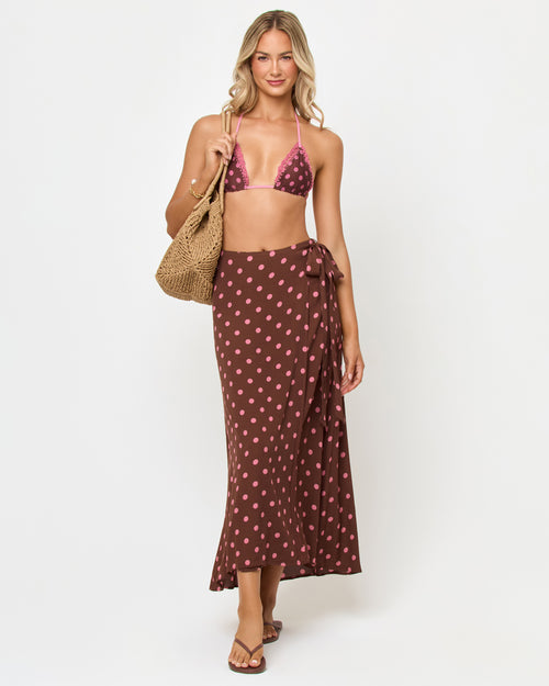 Front view of a model wearing the LSPACE Ever Wrap Skirt in alotta polka dot, a brown and pink polka dot midi wrap skirt with a side-tie detail, styled with a matching bikini top.