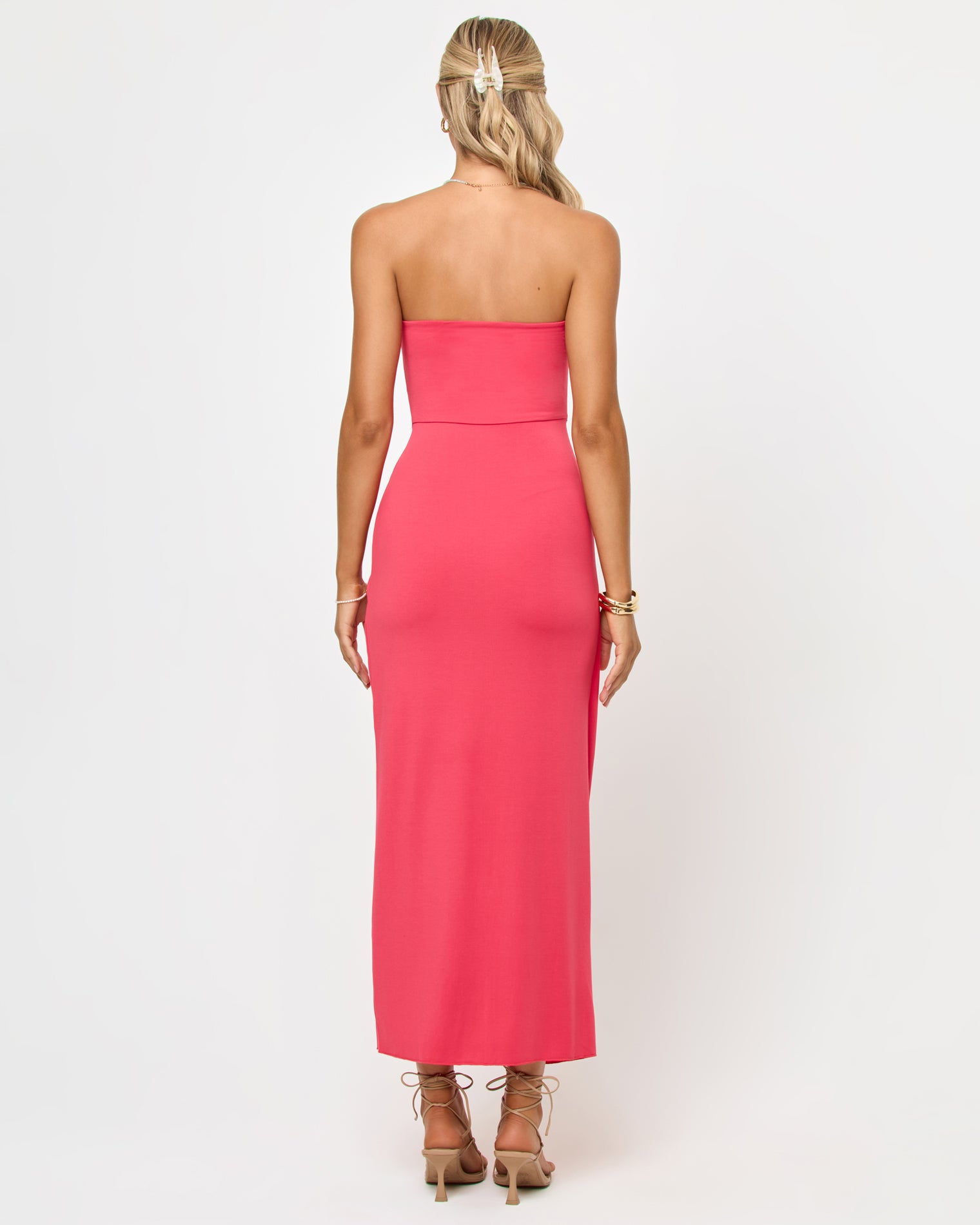 Noah Dress - Pout Back view of a model wearing the LSPACE Noah Dress in pout, showing the open strapless back in coral pink and the flowing maxi skirt.