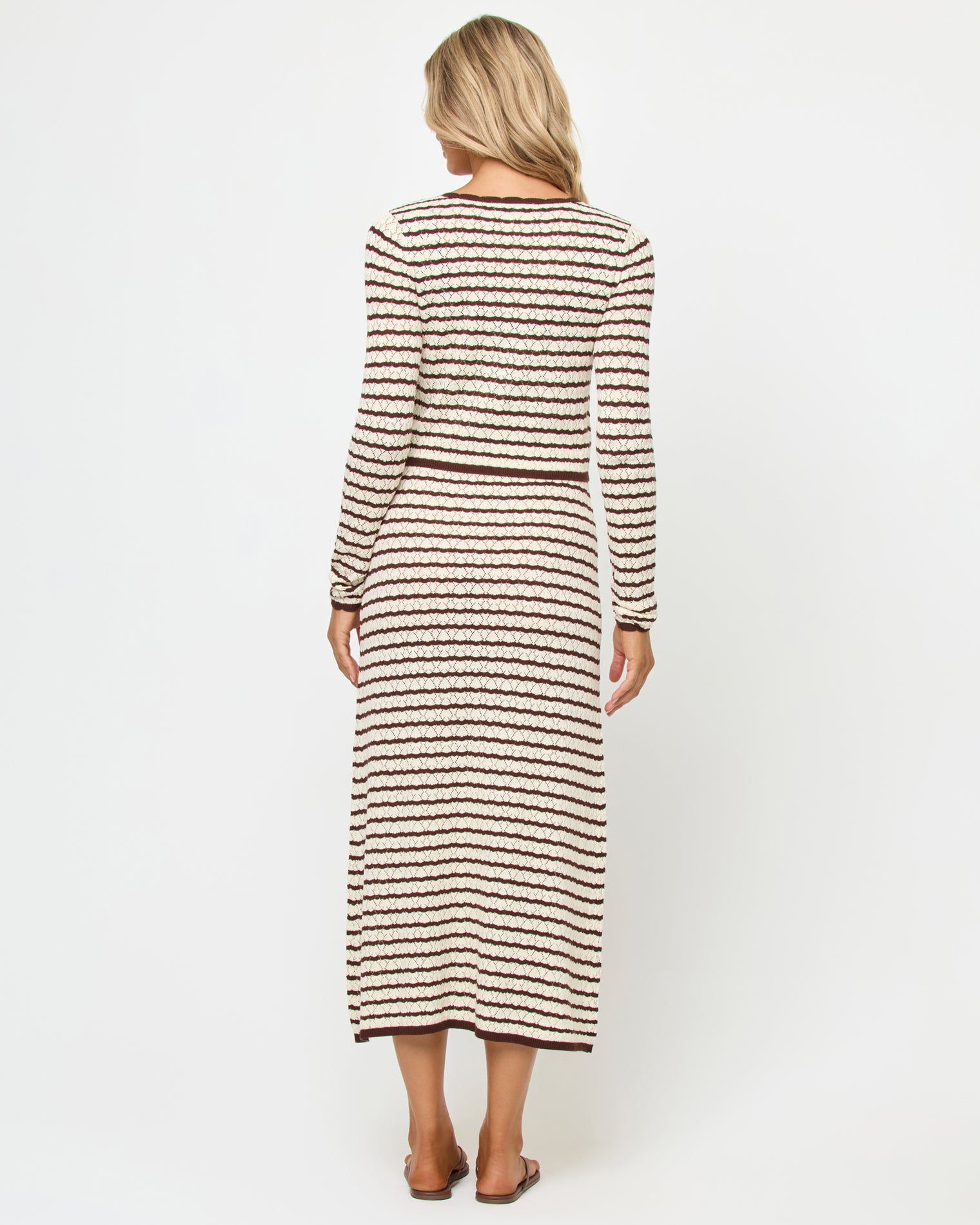 Rosalie Cardigan - Cafe-Cream Back view of a model wearing the LSPACE Rosalie Cardigan in cafe-cream, a cropped knit cardigan with cream and dark brown horizontal stripes, styled with the matching Rosalie Maxi dress.