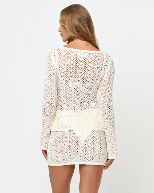 Back view of a model wearing the LSPACE Nova Top in cream, showing the long-sleeve crochet back with an open diamond lace pattern, styled with the matching LSPACE Nova Skirt.