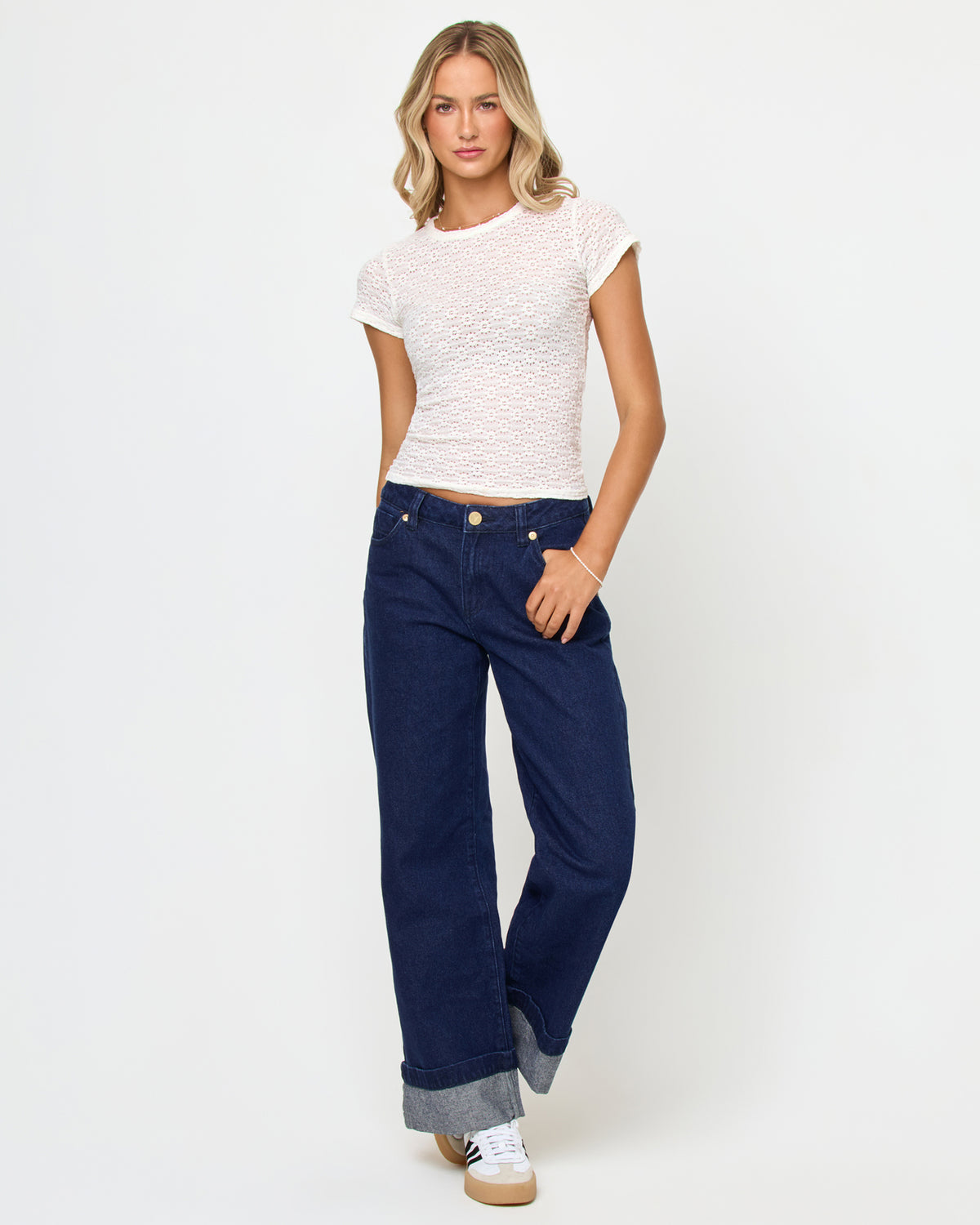 Lily Rose Top - Cream Full-length front view of a model wearing the LSPACE Lily Rose Top in cream, a fitted short-sleeve lace-textured crop top with a crew neckline, styled with wide-leg dark jeans and sneakers.