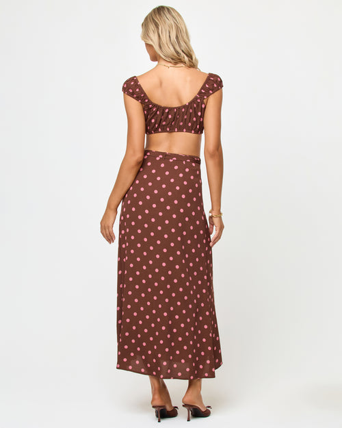Back view of a model wearing the LSPACE Ever Top in alotta polka dot, showing the open back of the brown and pink polka dot cap-sleeve crop top, paired with the matching wrap skirt.