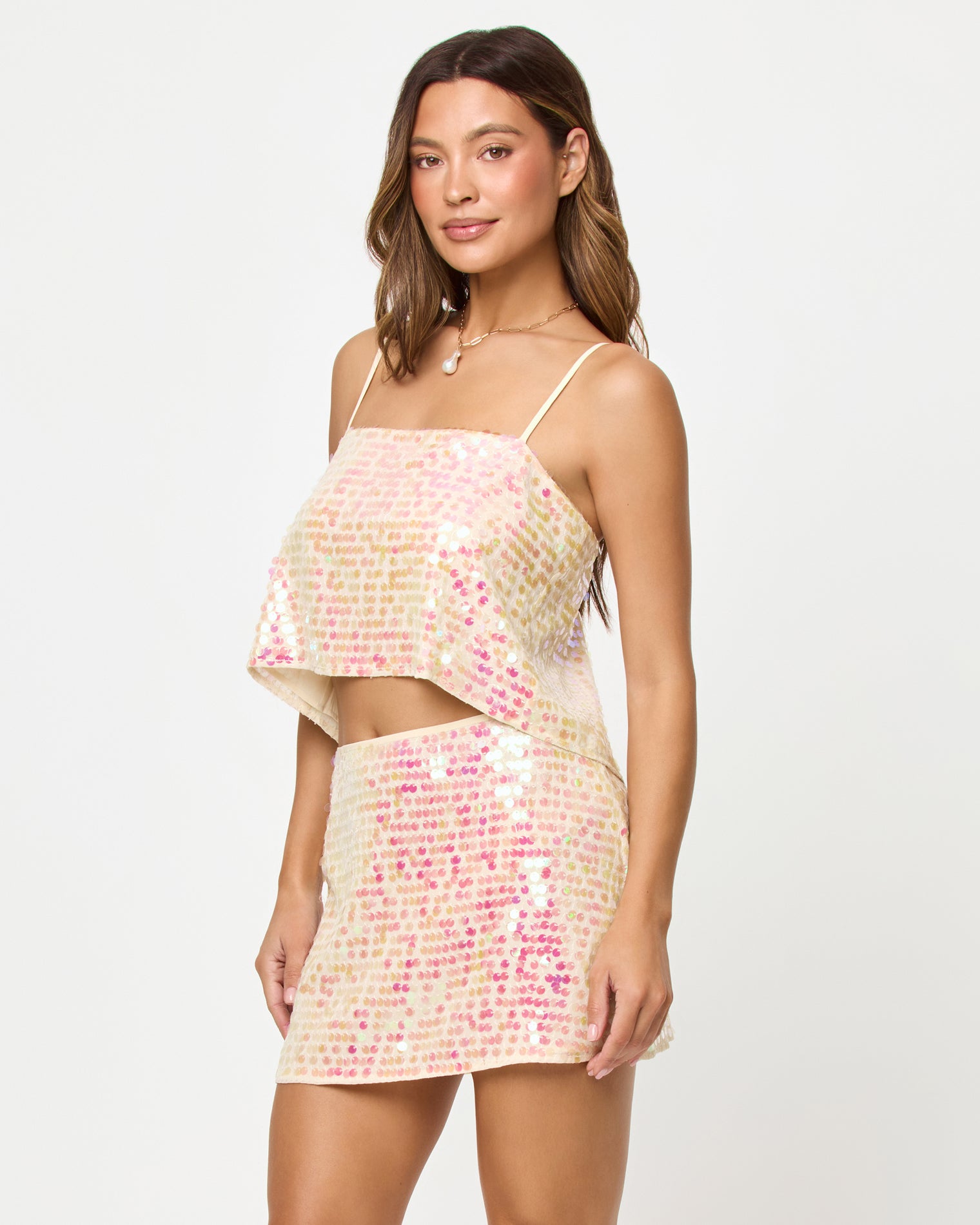 Glow Getter Top - Prosecco Three-quarter front view of a model wearing the LSPACE Glow Getter Top and Skirt in prosecco, an iridescent sequin mini skirt in champagne and pink tones.