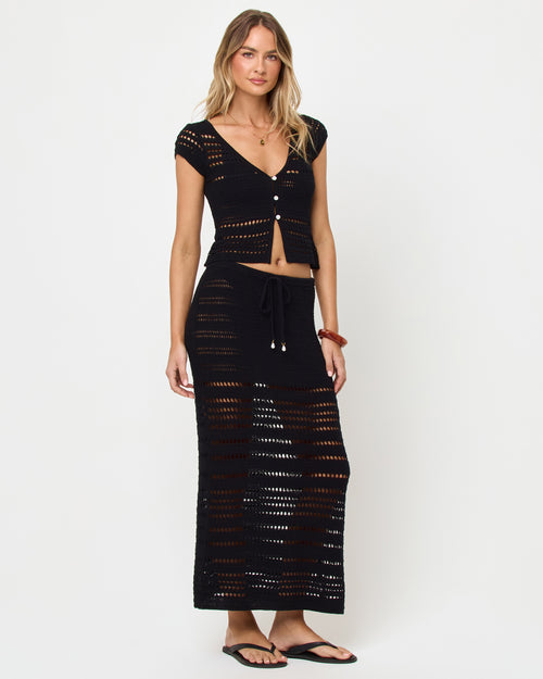 Side view of model wearing the LSPACE Tula Top in black, a semi-sheer crochet cropped top with cap sleeves with the mathcing Skirt.