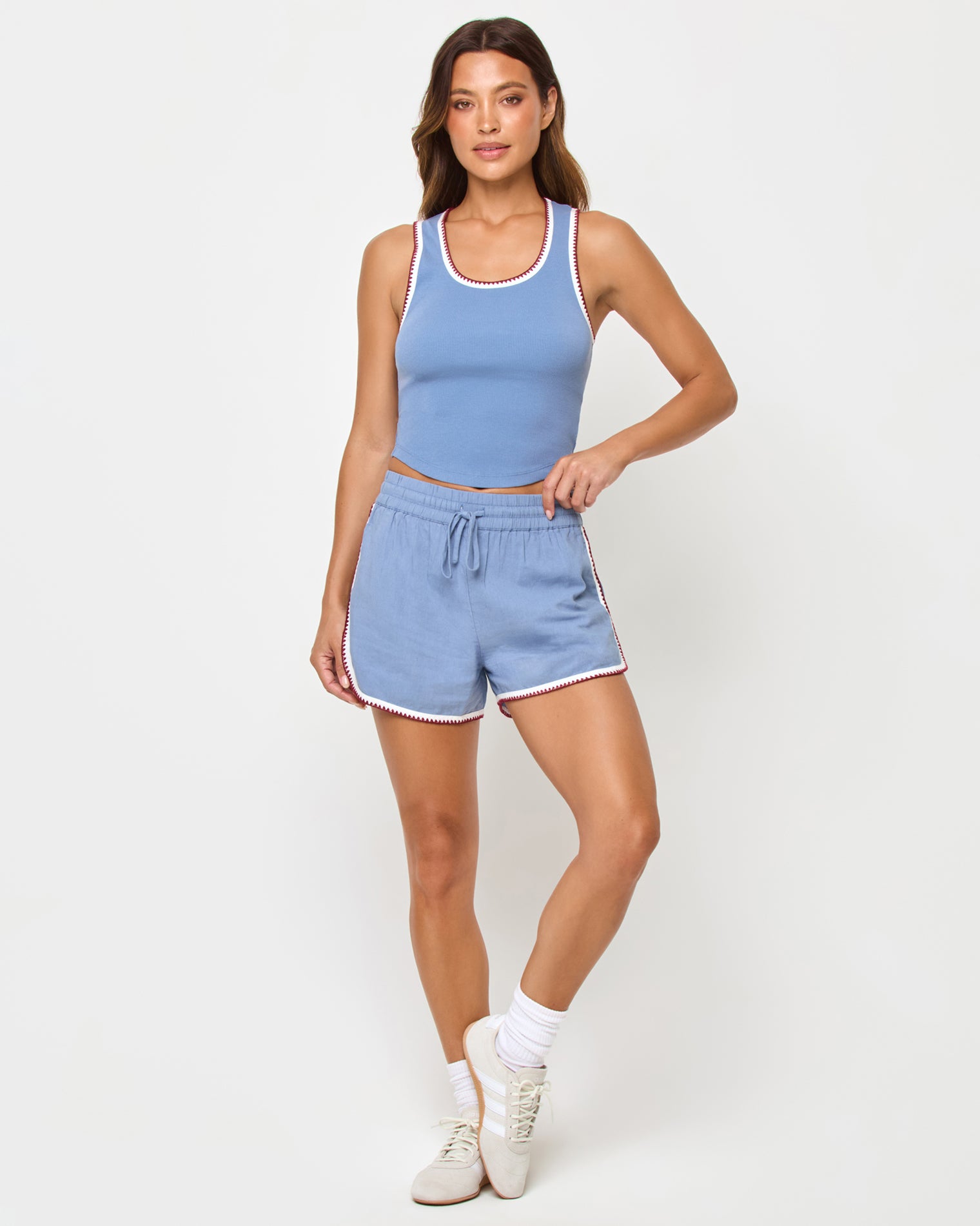 Rune Short - Cream Chambray Fig Front full-length studio view of the Ash Tank and Rune Short in Cream-Chambray-Fig, a chambray blue ribbed scoop-neck crop tank with white and burgundy crochet trim paired with matching chambray blue runner shorts with the same crochet trim, white crew socks, and cream sneakers.