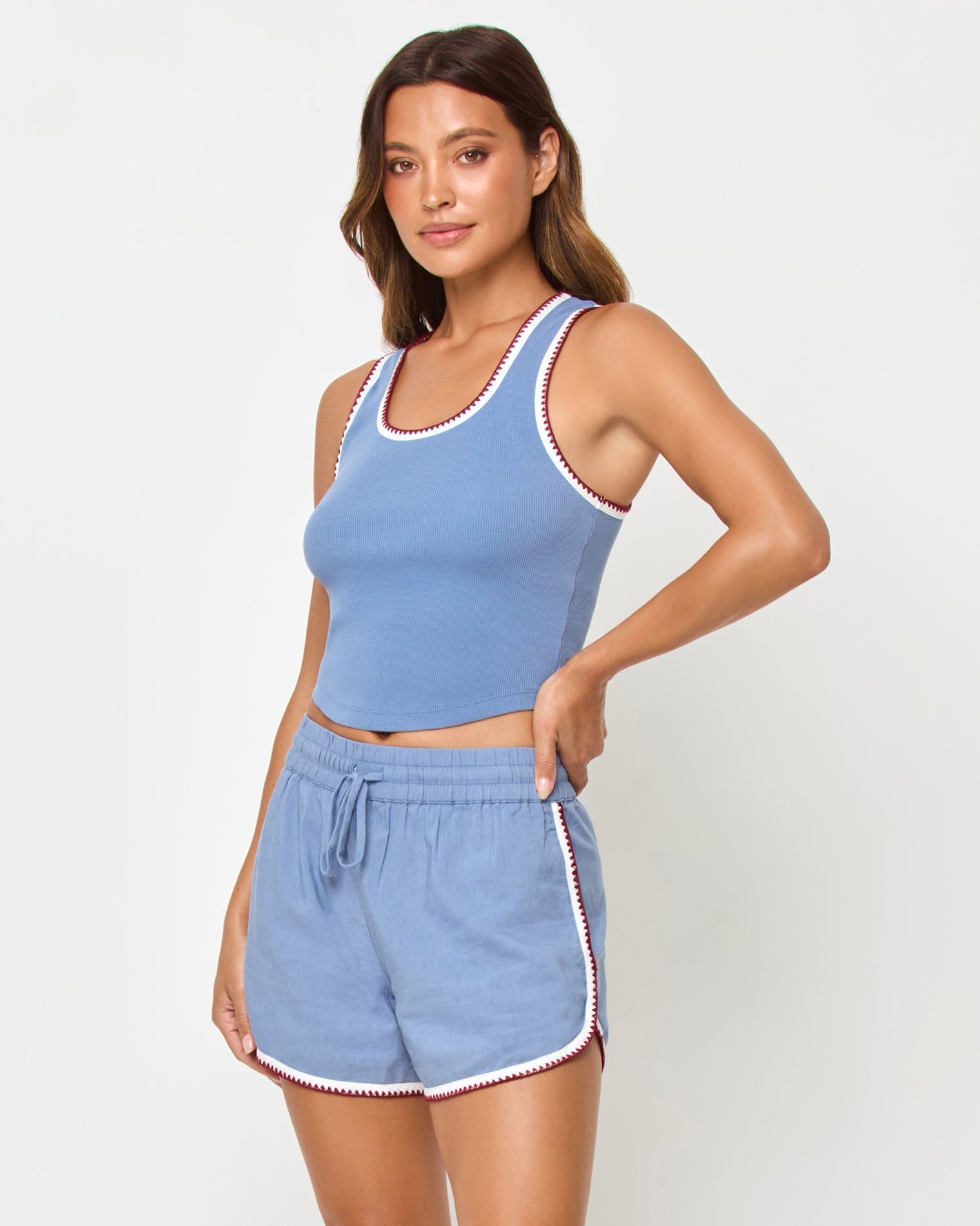Three-quarter side front studio view of the Ash Tank and Rune Short in Cream-Chambray-Fig, a chambray blue ribbed scoop-neck crop tank paired with matching chambray blue runner shorts with a drawstring waist, hand on hip.