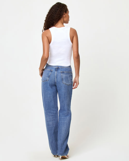 Back view of a model wearing the LSPACE Ash Tank in muah, showing the racerback detail of the white cropped ribbed tank, styled with light wash blue wide-leg jeans.