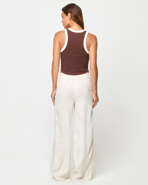 Back view of a model wearing the LSPACE Ash Tank in espresso-cream, showing the racerback detail with cream contrast trim against the espresso brown body, styled with cream wide-leg drawstring pants.