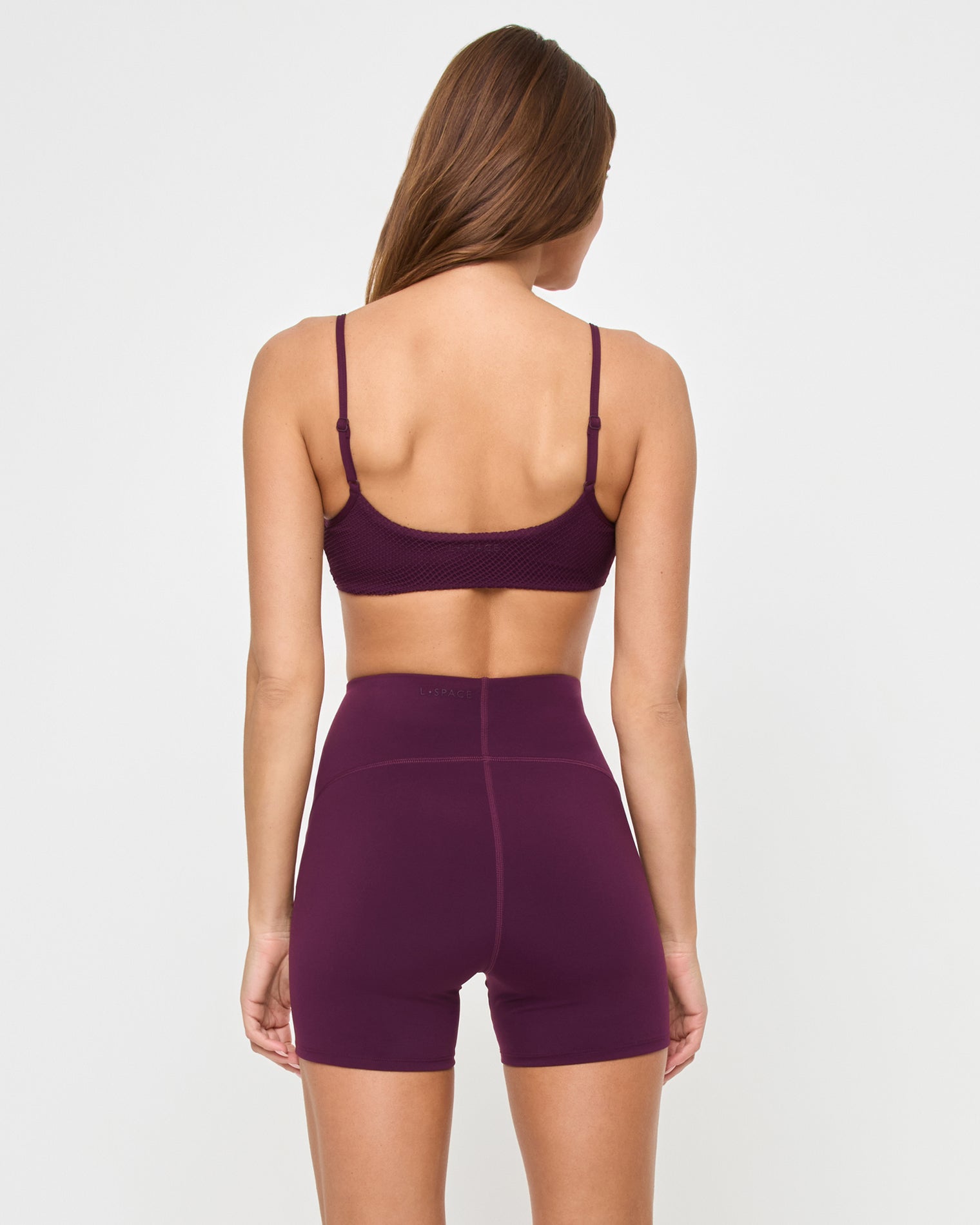 En Pointe Short - Plum Back view of the LSPACE En Pointe Short in plum on a model against a white background, showing the back of the high-waist active shorts, paired with the matching plum Stride Bra.