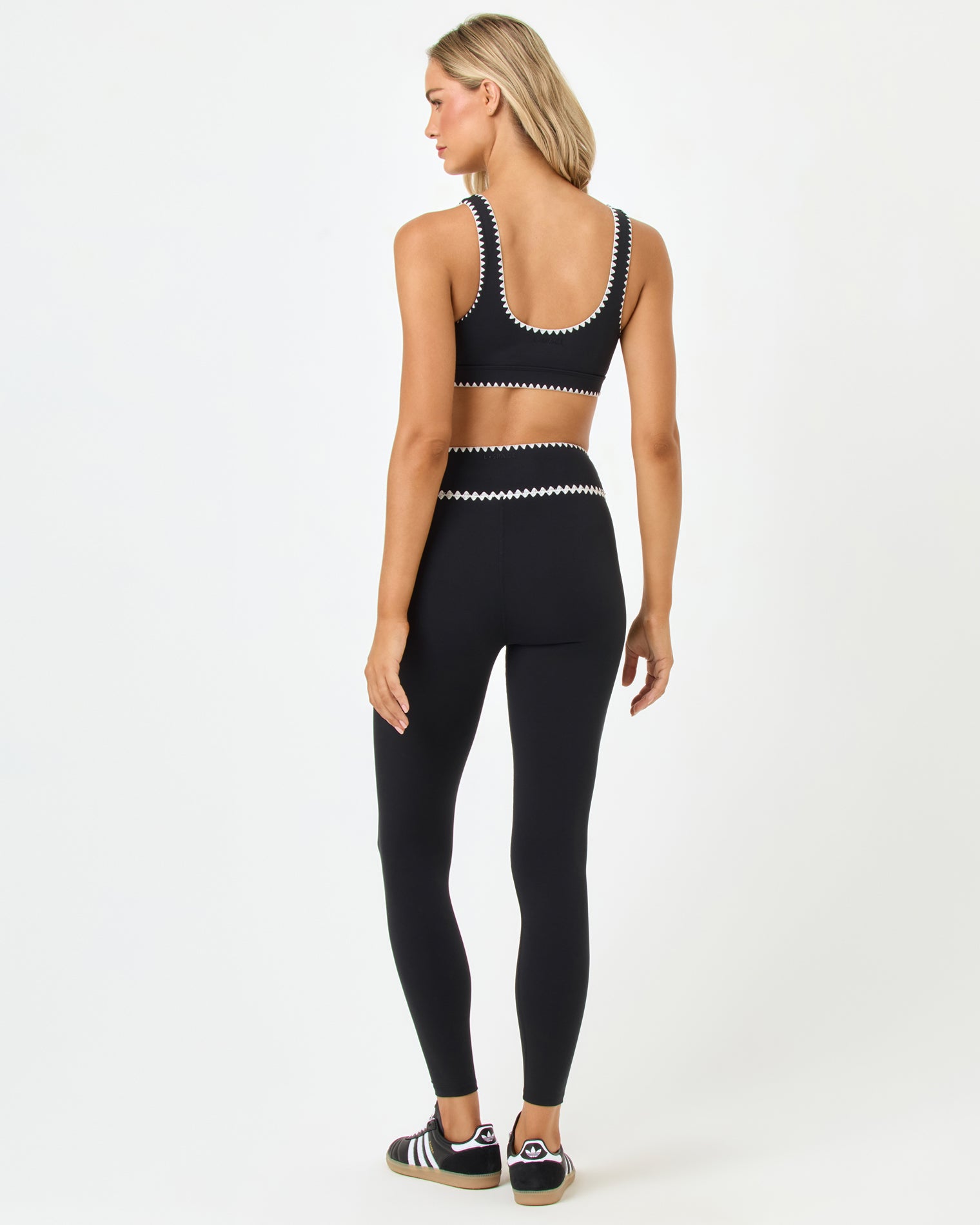 Heartbreaker Legging - Black Back full-length studio view of the Heartbreaker Bra and Legging in black, a black sports bra with white zig-zag trim at the back and underbust band paired with matching black high-waist leggings with white zig-zag trim at the waist, styled with Adidas sneakers.