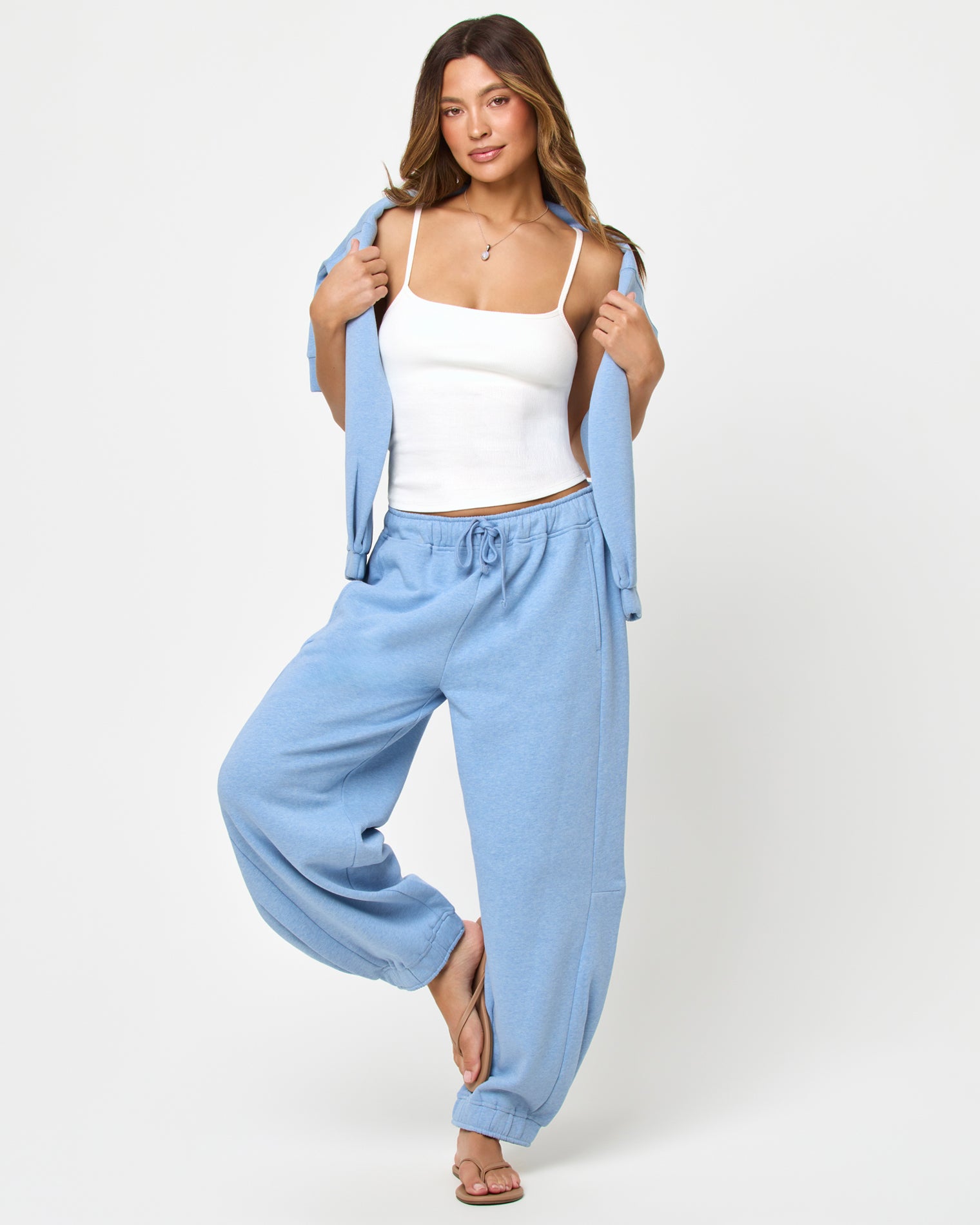 Fleur Sweatshirt - Chambray Front full-length studio view of the Fleur Pant in chambray blue, chambray blue wide-leg drawstring jogger pants with cuffed ankles, styled with a white spaghetti-strap tank and a chambray blue open-front cardigan held open, tan flip flops.