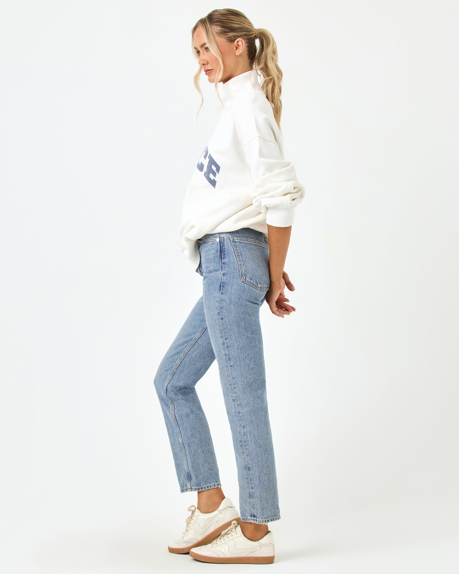Crush Sweatshirt - Cream Side profile full-length studio view of the Crush Sweatshirt in cream, a cream quarter-zip pullover sweatshirt with "LSPACE" collegiate arch lettering, styled with blue jeans and white sneakers.