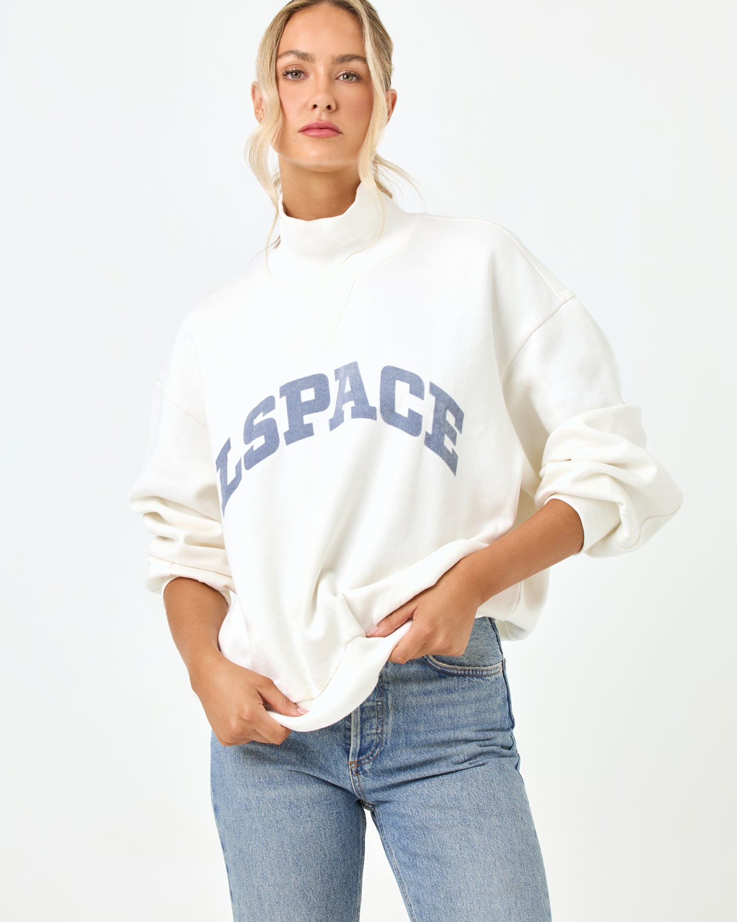 Crush Sweatshirt - Cream Studio torso view of the Crush Sweatshirt in cream, a cream quarter-zip pullover sweatshirt with "LSPACE" collegiate arch lettering, styled with light blue denim jeans.