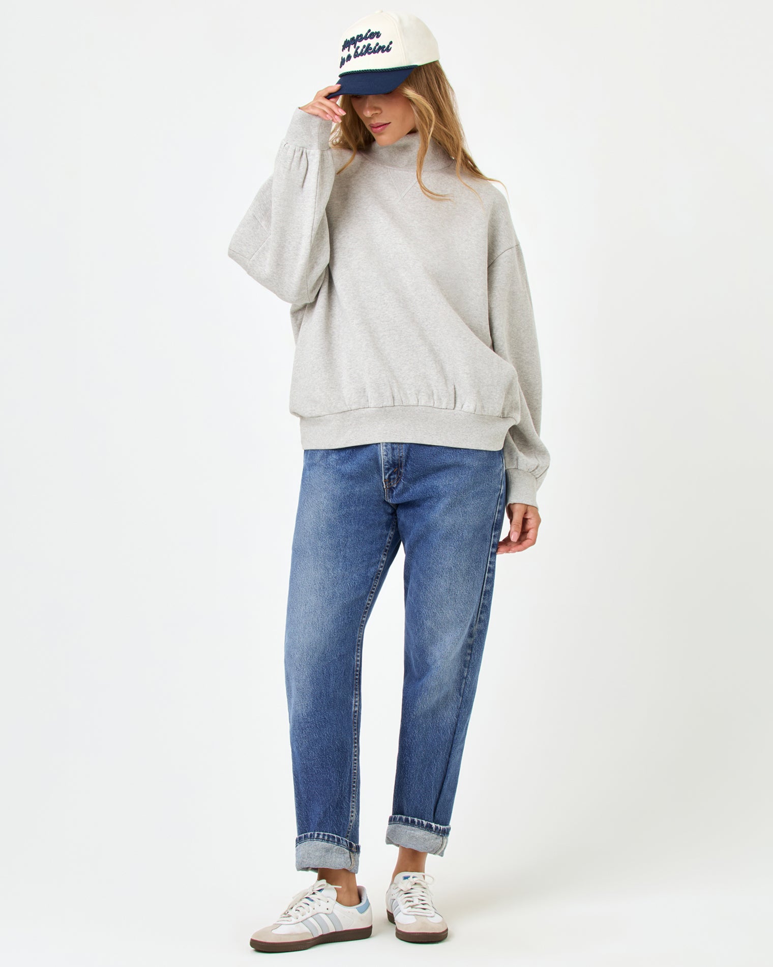 Crush Sweatshirt - Heather Gray Front full-length studio view of the Crush Sweatshirt in Heather Gray, a heather gray oversized quarter-zip sweatshirt, styled with cuffed blue jeans, Adidas sneakers, and a navy and cream baseball cap.