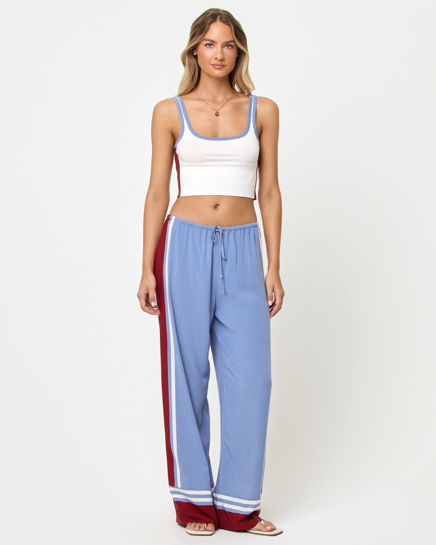 Unwind Pant - Unwind Stripe Front full-length studio view of the Reset Tank and Unwind Pant in Cream-Chambray-Fig, a cream ribbed scoop-neck crop cami with chambray blue and burgundy trim and color-block sides paired with chambray blue wide-leg stripe pants with a burgundy side stripe and cream piping, stripe trim at the ankles, styled with nude heeled sandals.