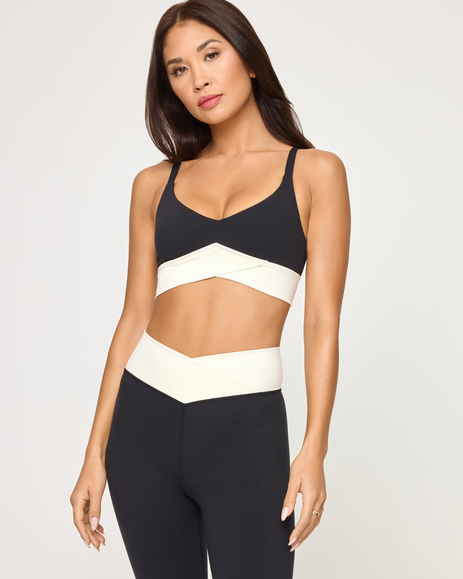 Unmatched Legging - Black-Cream Close-up front view from the waist up of the LSPACE Unmatched Legging in black-cream on a model against a white background, highlighting the cream crossover band detail of the matching bra and the cream crossover waistband of the leggings.