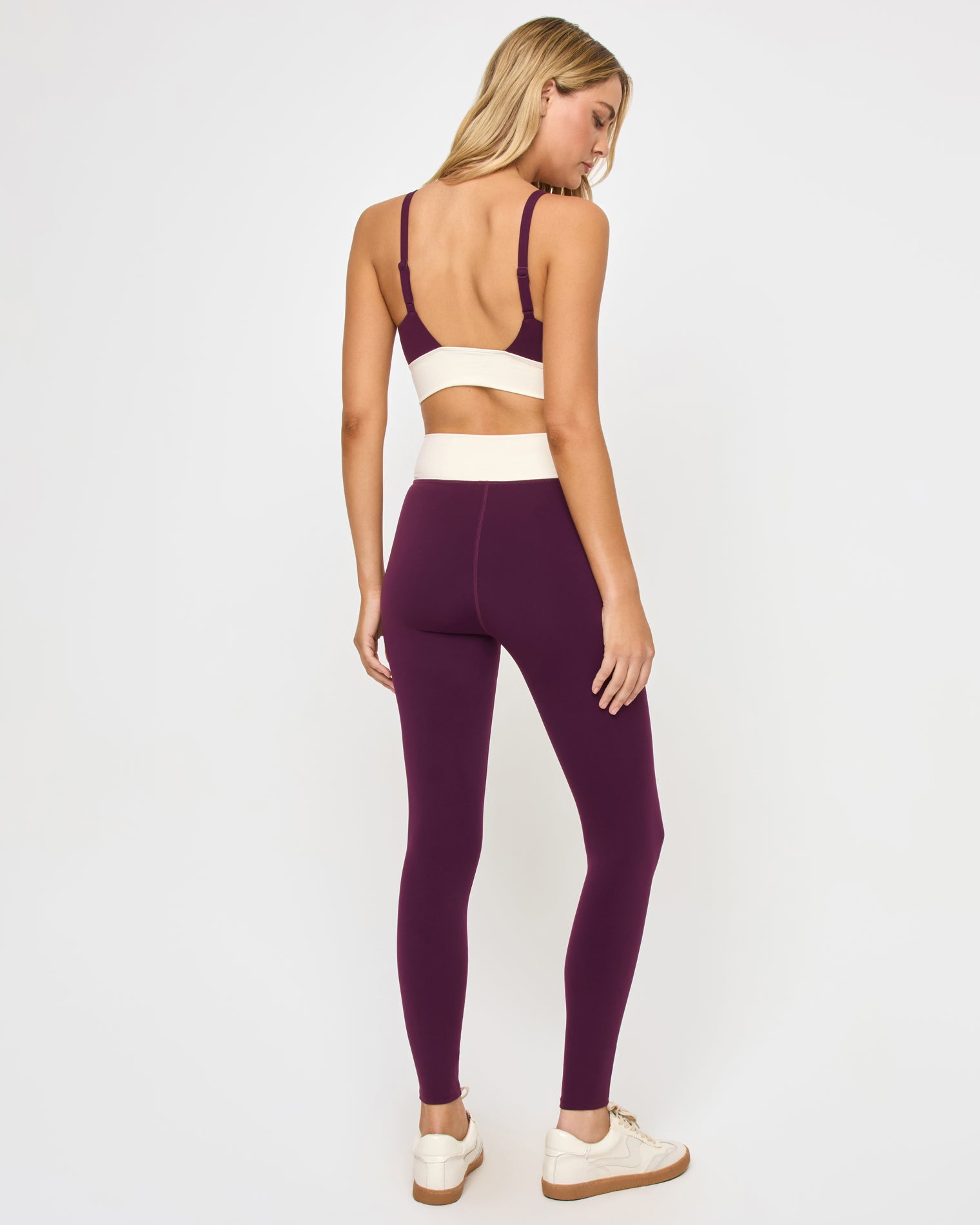 Unmatched Legging - Plum-Cream Back view of the LSPACE Unmatched Legging in plum-cream on a model against a white background, showing the cream crossover waistband and the open back of the matching plum triangle sports bra with thin straps, with cream sneakers.