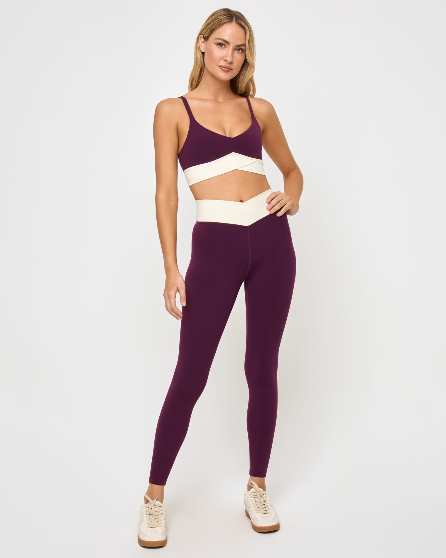 Unmatched Legging - Plum-Cream Front view of the LSPACE Unmatched Legging in plum-cream on a model against a white background, showing the high-rise full-length leggings with a cream crossover waistband, paired with the matching plum triangle sports bra and cream sneakers.