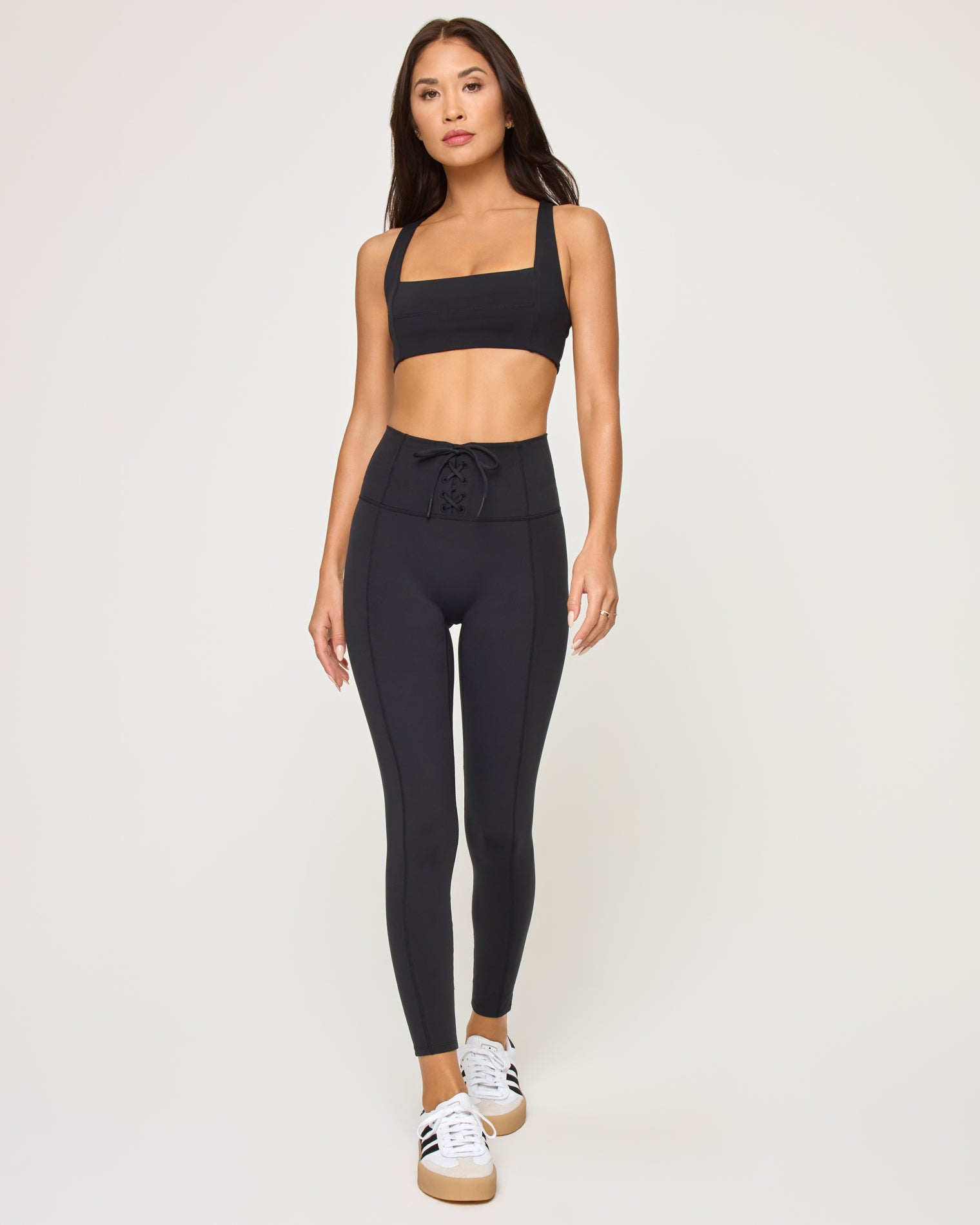 Contender Legging - Black Front view of model wearing the Contender Legging in black, a high-waist legging with seam detail, with matching black sports bra and white sneakers.