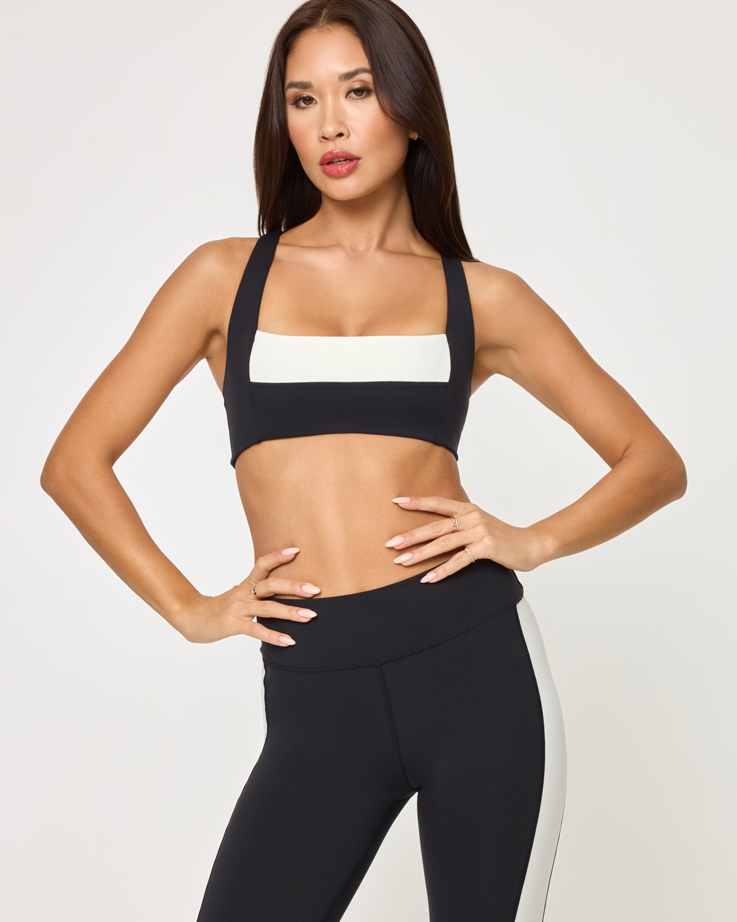 Uppercut Bra - Black-Cream Lifestyle editorial shot of a model wearing the LSPACE Uppercut Bra in black-cream paired with matching black-cream high-rise active pants, in an outdoor setting.