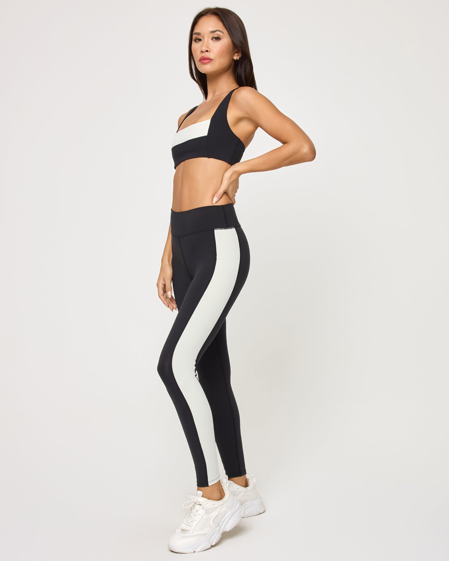 Uppercut Bra - Black-Cream Side view of the LSPACE Uppercut Bra in black-cream on a model against a white background, paired with black-cream high-rise active pants, showing the profile of the matching outfit.