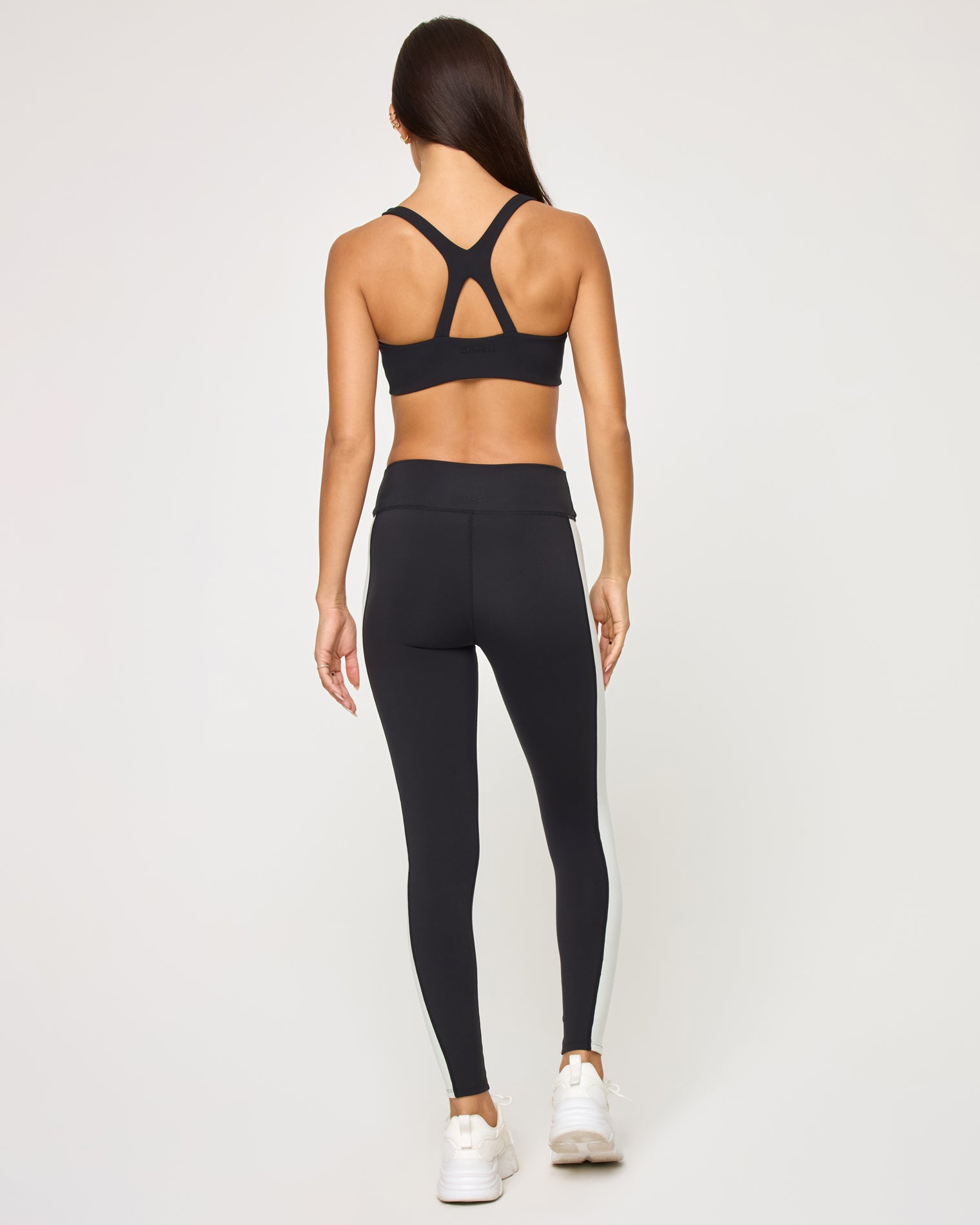 Uppercut Bra - Black-Cream Back view of the LSPACE Uppercut Bra in black-cream on a model against a white background, showing the crossback strap detail, paired with black-cream high-rise active pants.