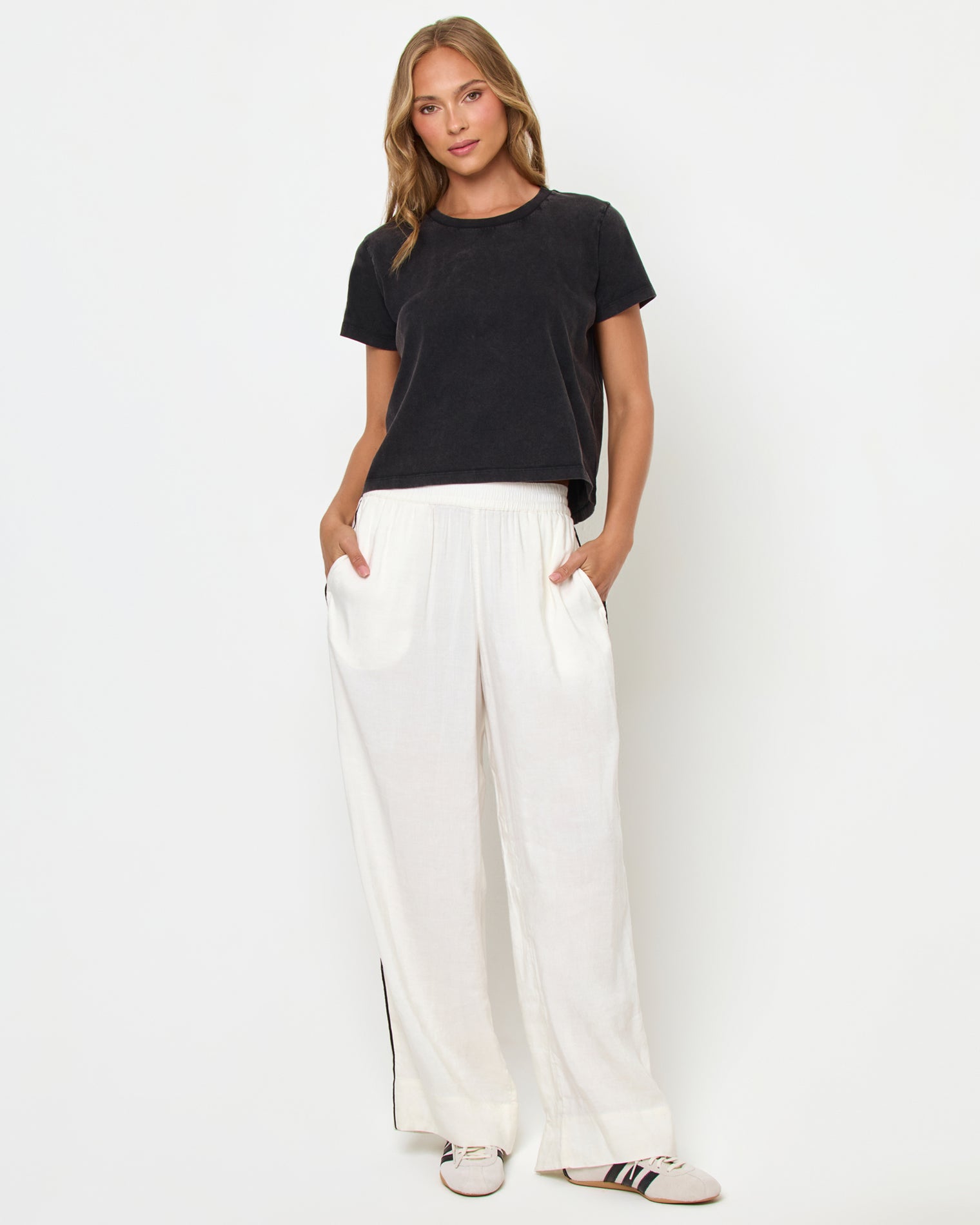All Day Top - Black Full body front view of a model wearing the LSPACE All Day Top in black, styled with white wide-leg track pants and sneakers.