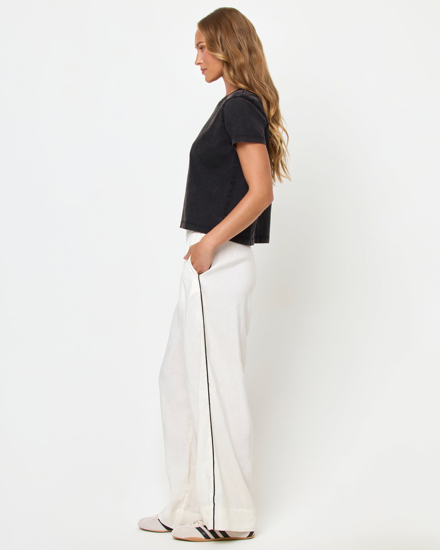 All Day Top - Black Side view of a model wearing the LSPACE All Day Top in black, styled with white wide-leg track pants.
