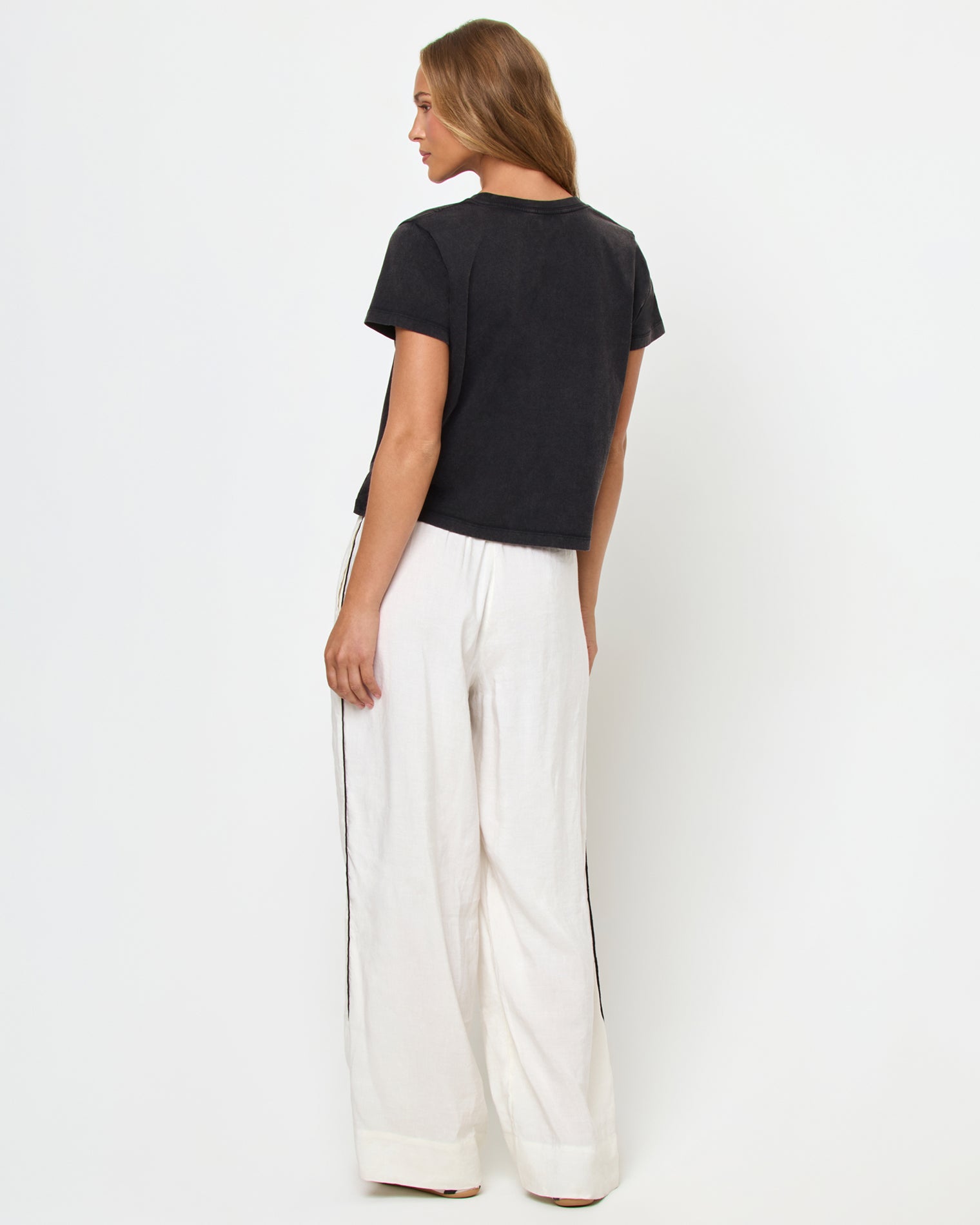 All Day Top - Black Back view of a model wearing the LSPACE All Day Top in black, styled with white wide-leg track pants.