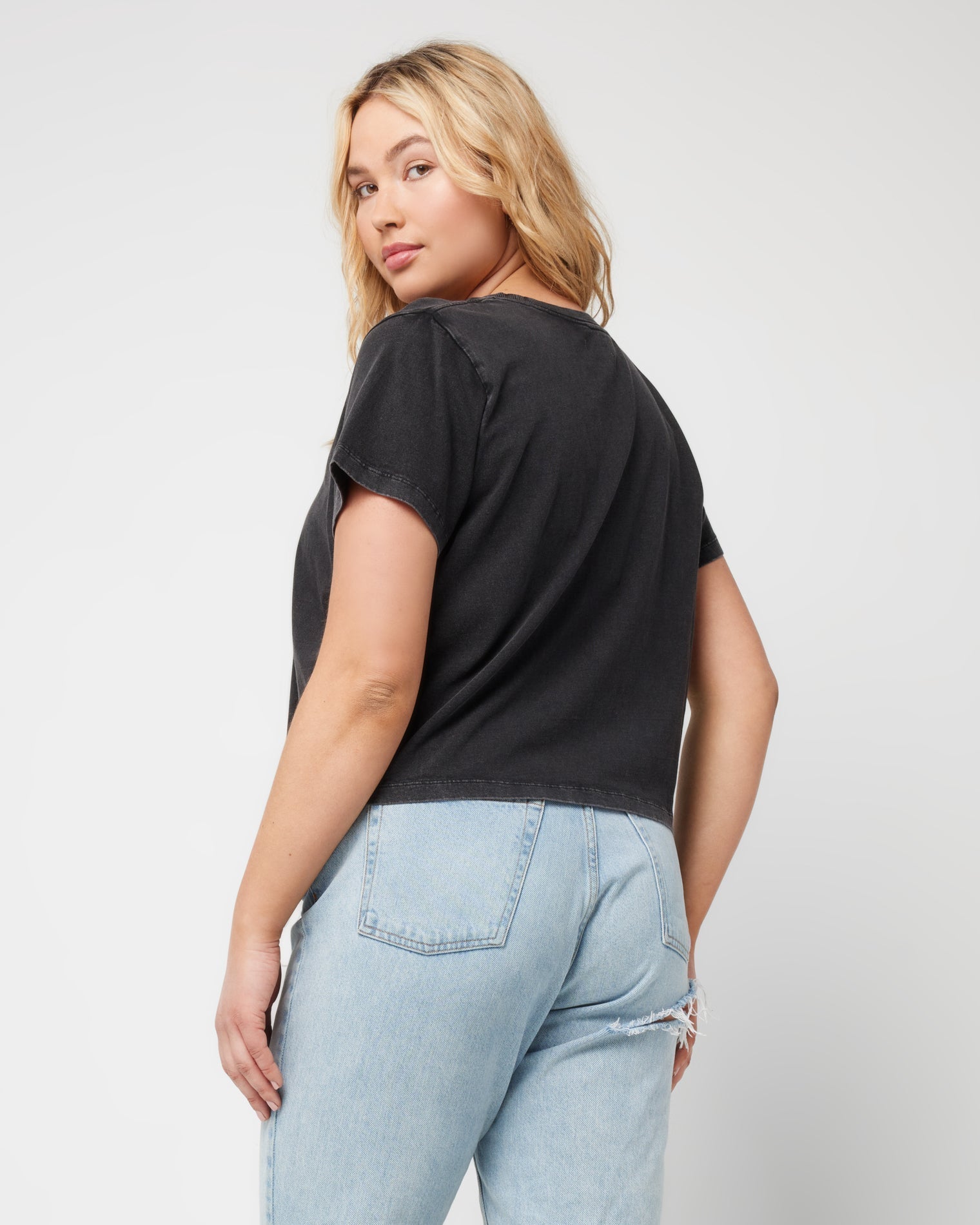 All Day Top - Black Angled back view of a model looking over her shoulder wearing the LSPACE All Day Top in black, styled with light wash jeans.