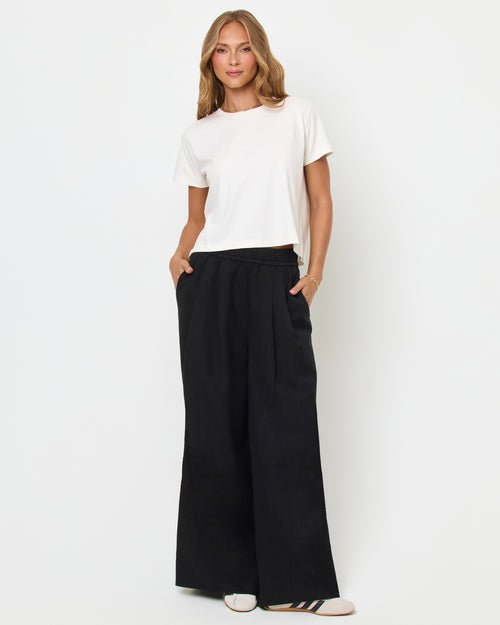 Full body front view of a model wearing the LSPACE All Day Top in cream, styled with black wide-leg pants with a cream side stripe and sneakers.