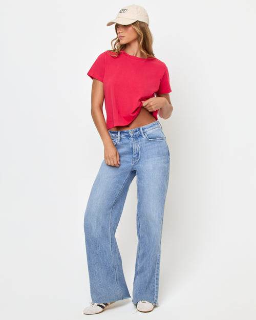 Three-quarter view of a model wearing the LSPACE All Day Top in pout, a cropped crew-neck tee with short sleeves, styled with light wash wide-leg jeans and a cream baseball cap.