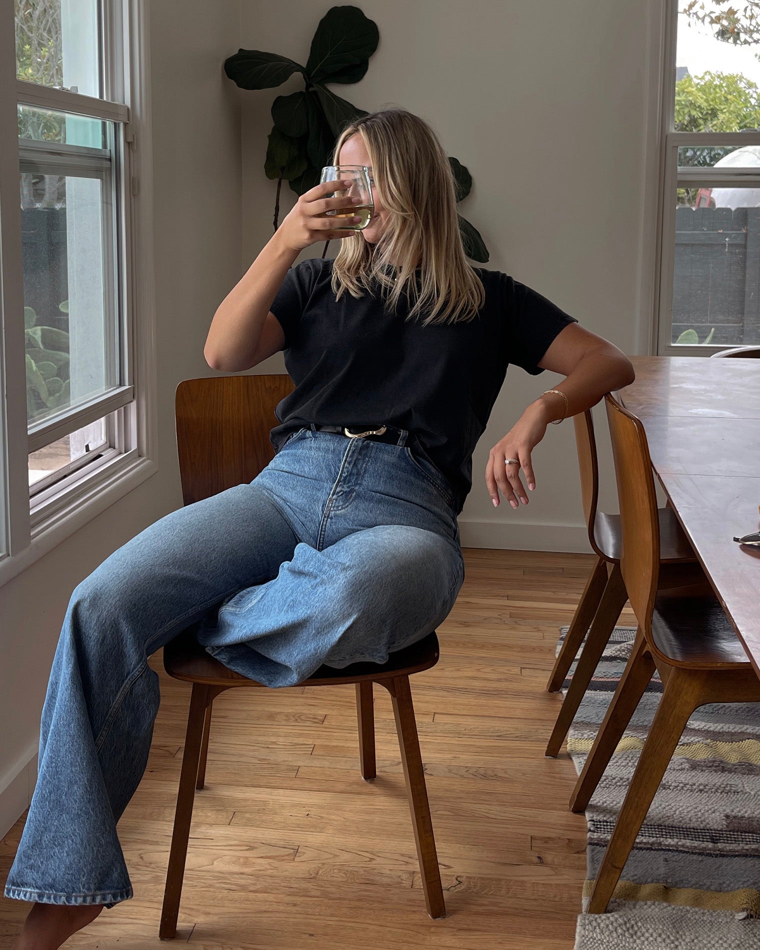 All Day Top - Black Lifestyle front view of a model seated at a dining table wearing the LSPACE All Day Top in black, styled with light wash wide-leg jeans.