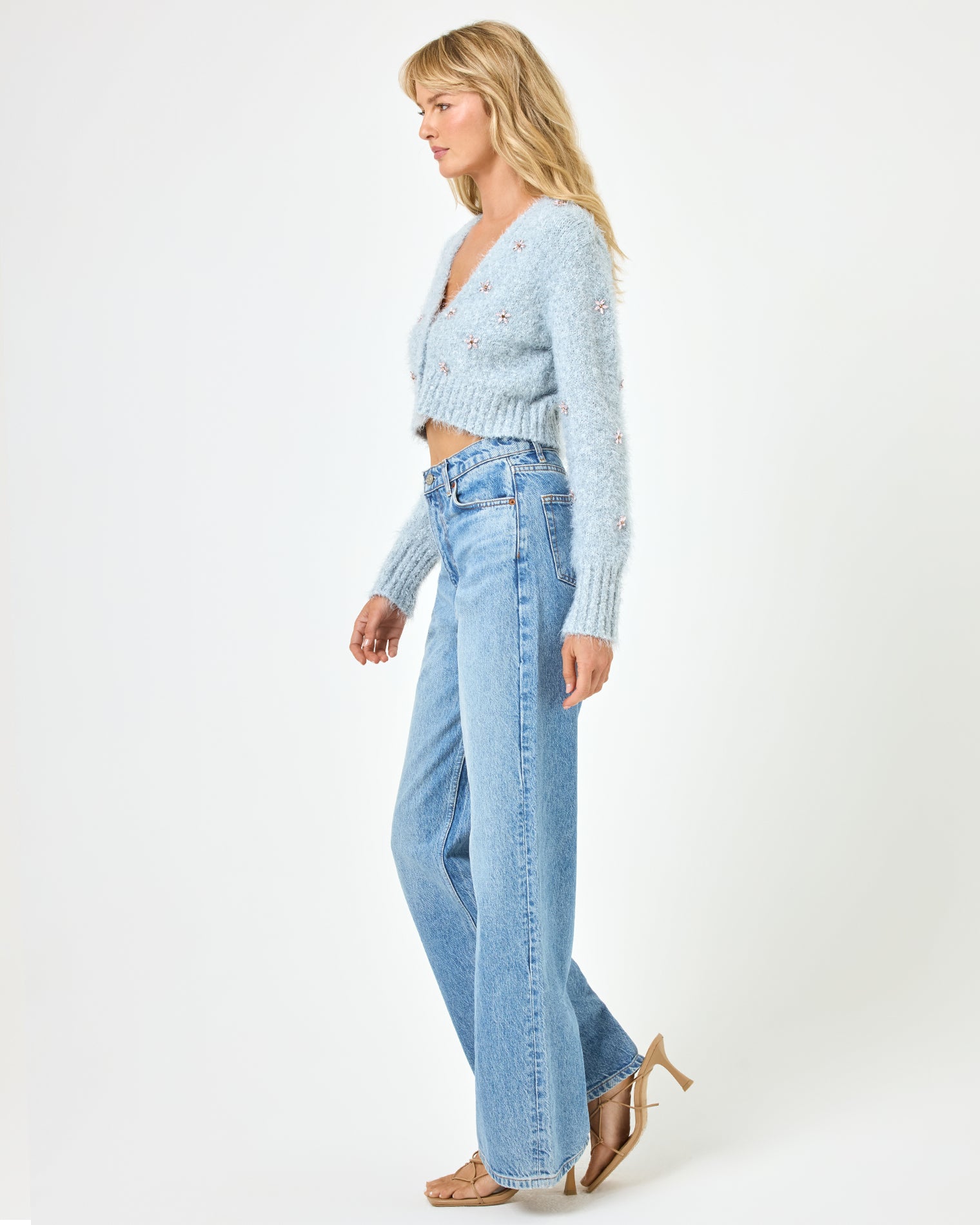 Crystal Cardigan - Dove Full body side view of a model wearing the LSPACE Crystal Cardigan in dove, showing the cropped silhouette and long sleeves of the fluffy knit cardigan with crystal floral embellishments, styled with wide-leg jeans.
