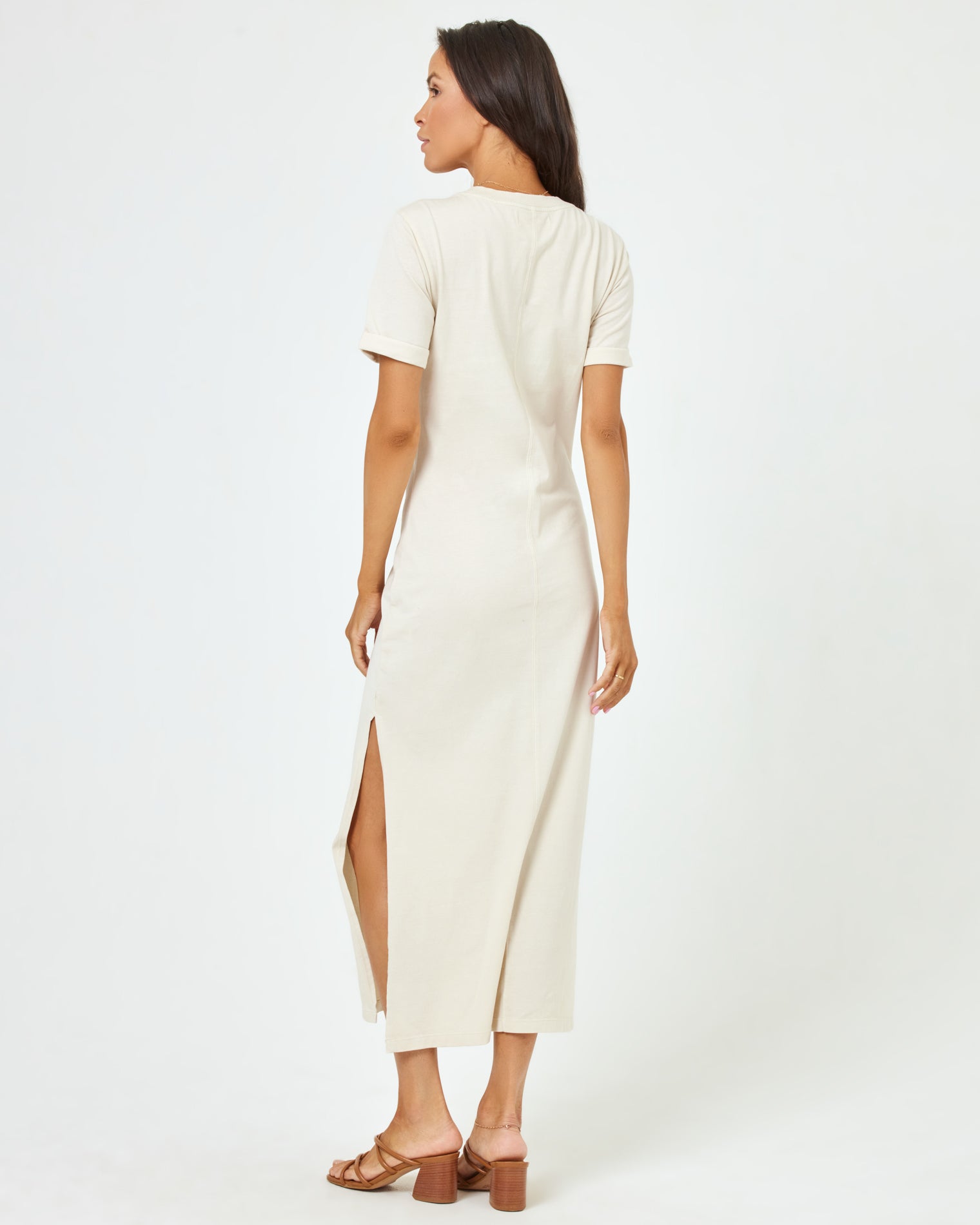 Drew Dress - Cream Back view of a model wearing the LSPACE Drew Dress in cream, a short-sleeve jersey midi dress with a side slit.